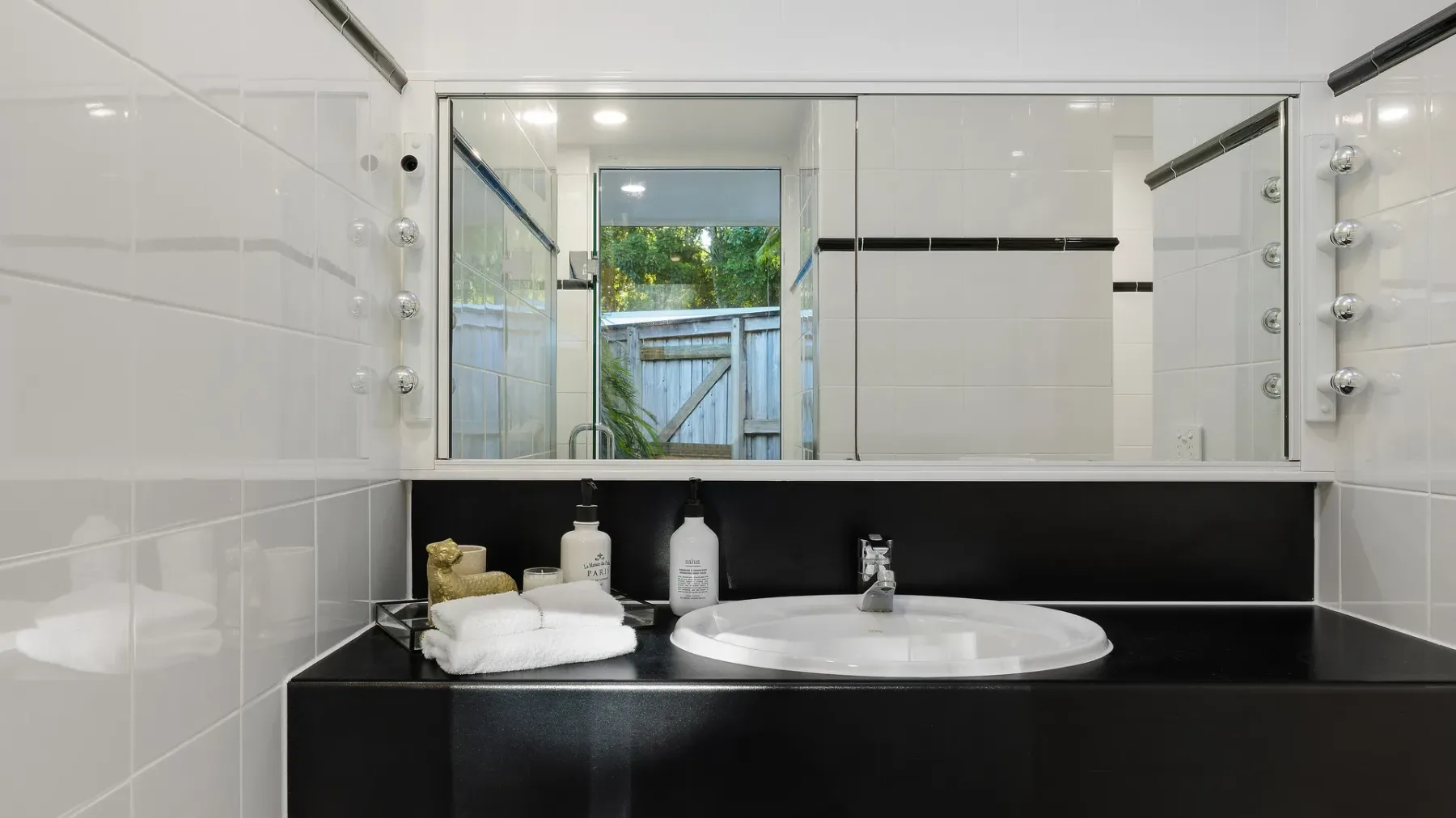 Un lavabo de baño con un espejo amplio, un lavamanos blanco y una encimera oscura.
