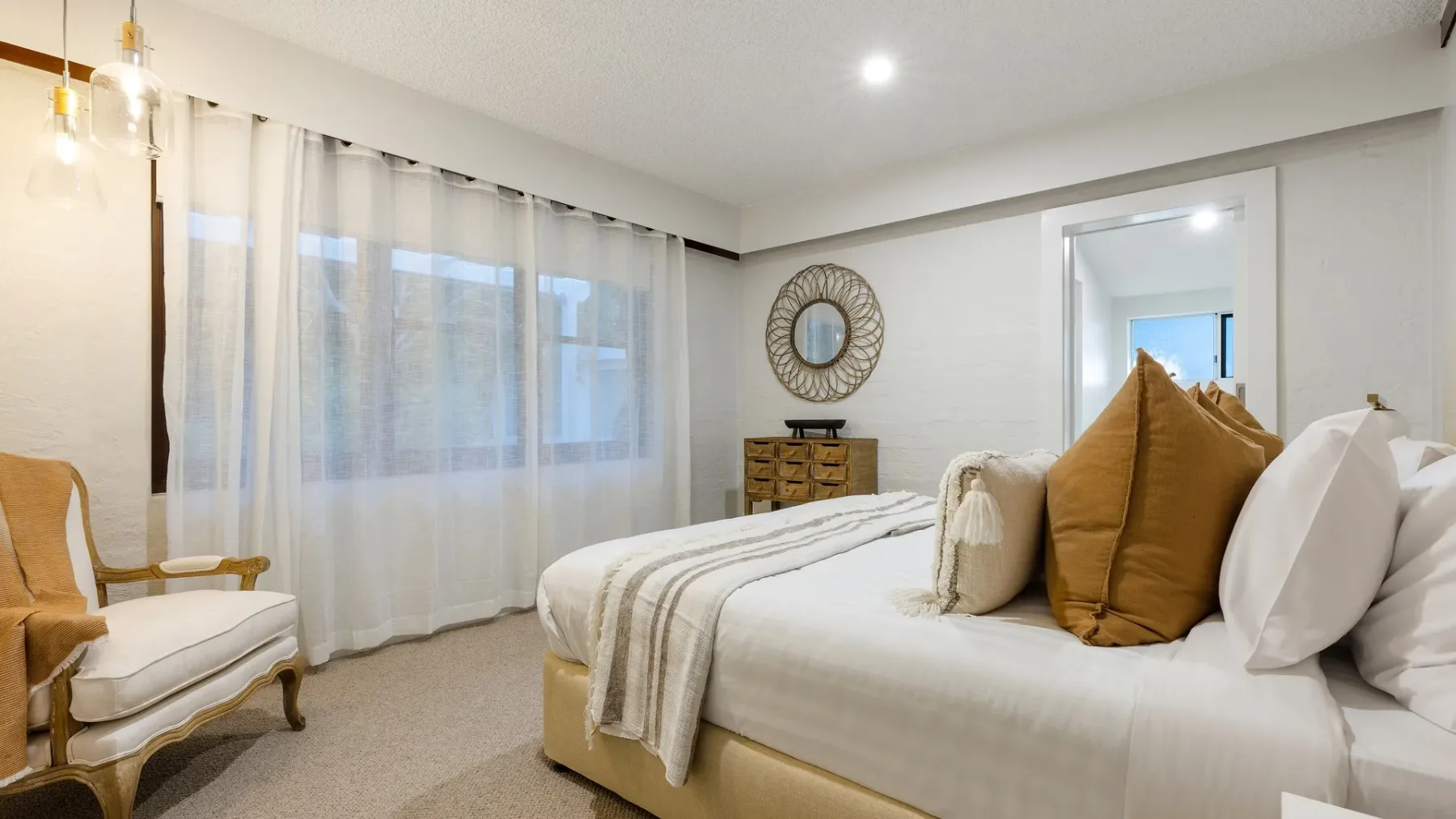 Un dormitorio con una cama bien arreglada, almohadas en capas y cortinas translúcidas.