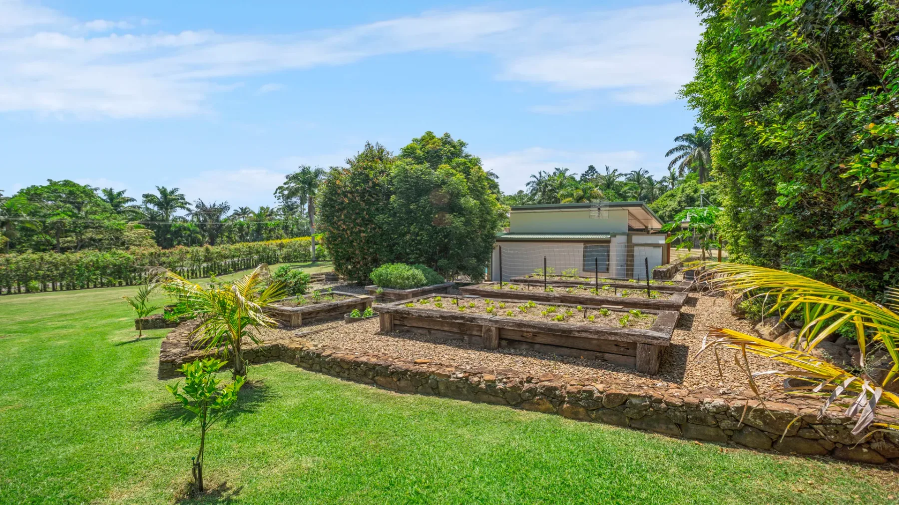 Un jardín ajardinado con bancales elevados de piedra y un pequeño edificio al fondo.