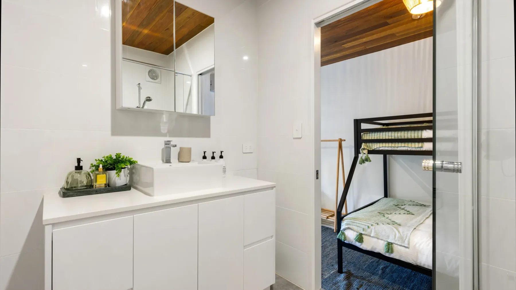 Un lavabo con espejo junto a una puerta abierta que da a un dormitorio.