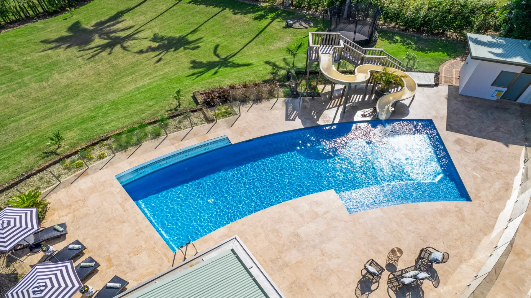 Una piscina al aire libre está junto a un patio pavimentado y un césped verde.