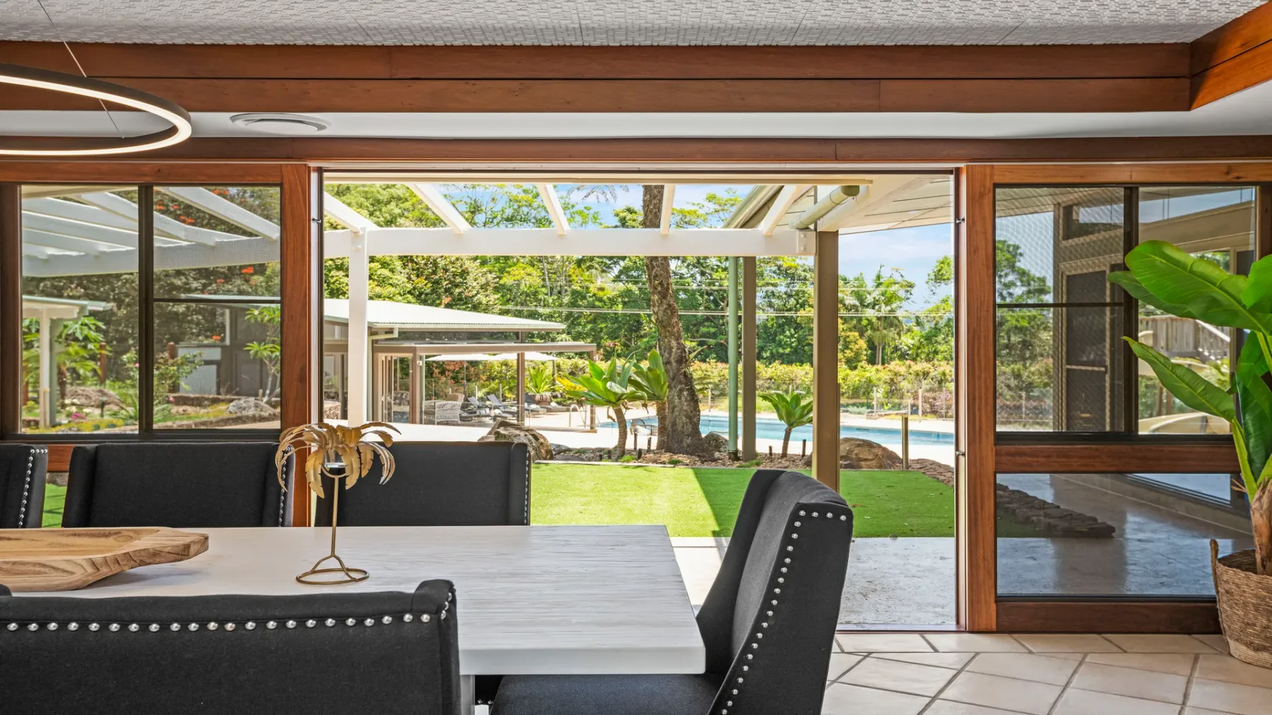 Un comedor se abre a un jardín y una piscina a través de grandes ventanales.