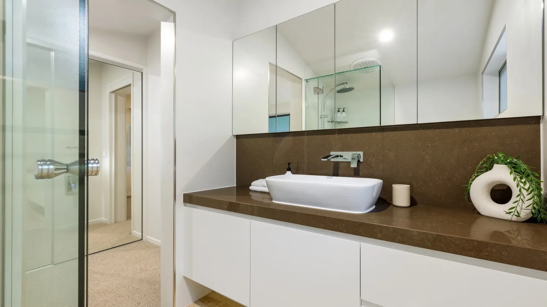 Un baño moderno con lavabo blanco sobre la encimera marrón y un espejo grande.