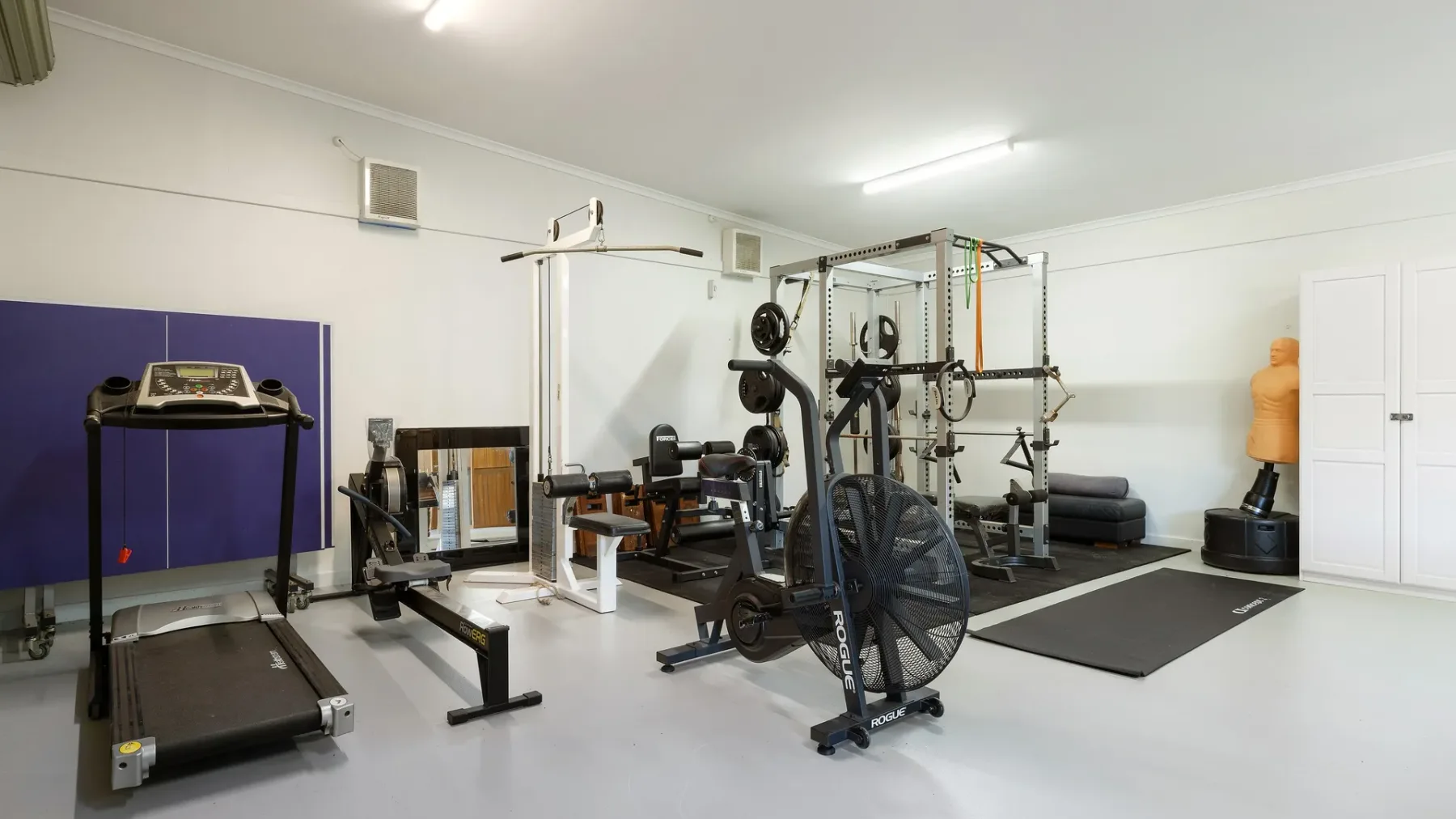 Un gimnasio en casa con máquinas de ejercicio, pesas y colchonetas.
