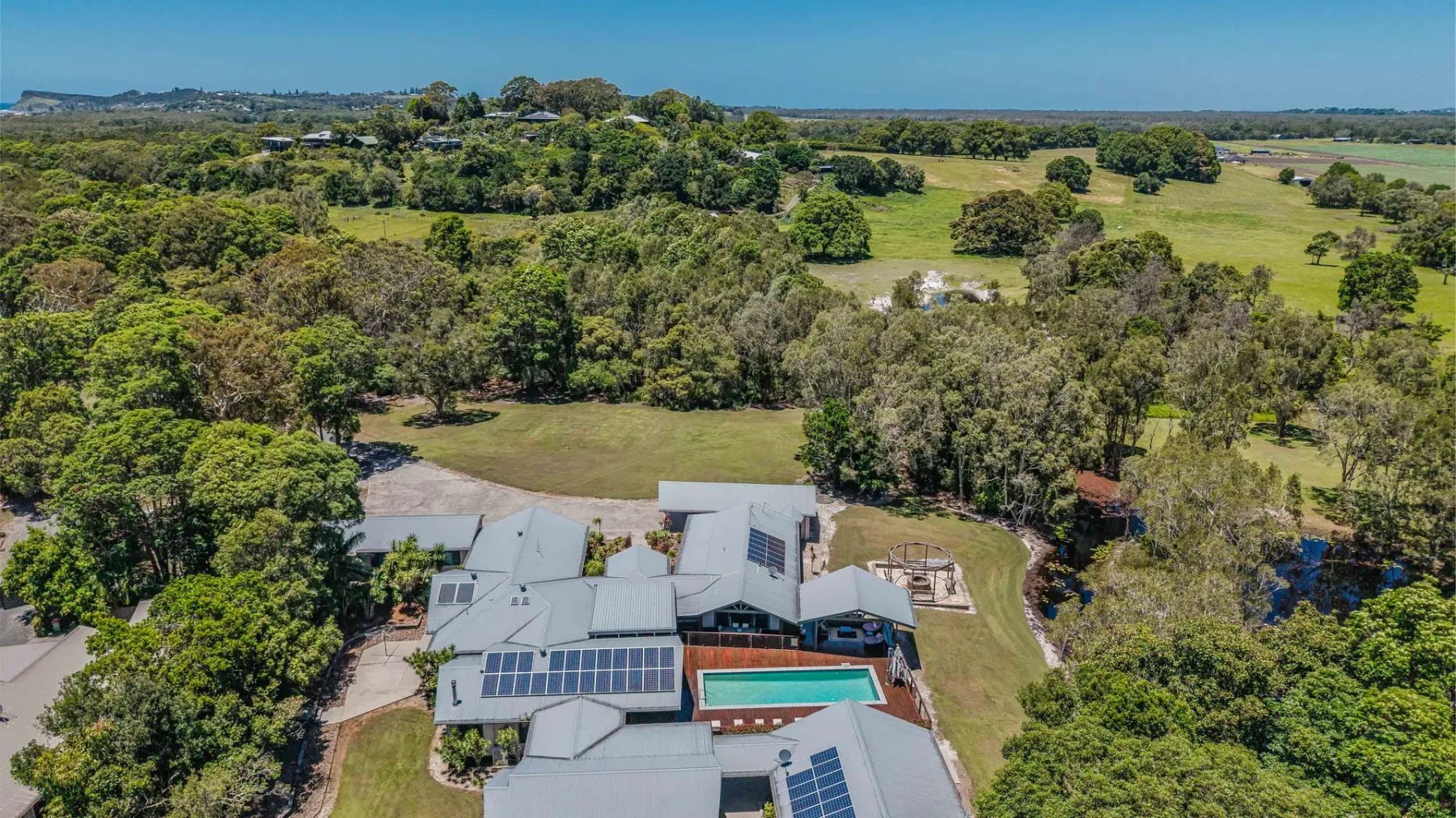 An aerial view of a house with solar panels and a swimming pool amid green countryside.