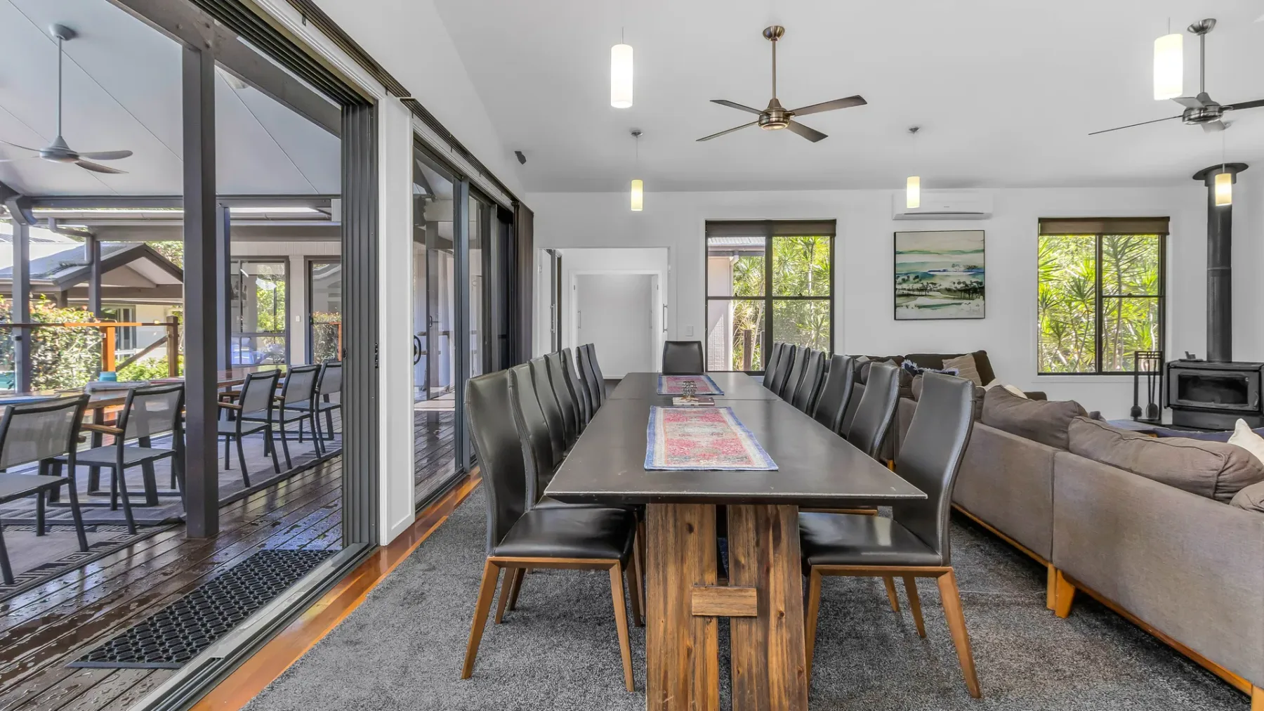 A dining area with a long table and seating beside large windows.