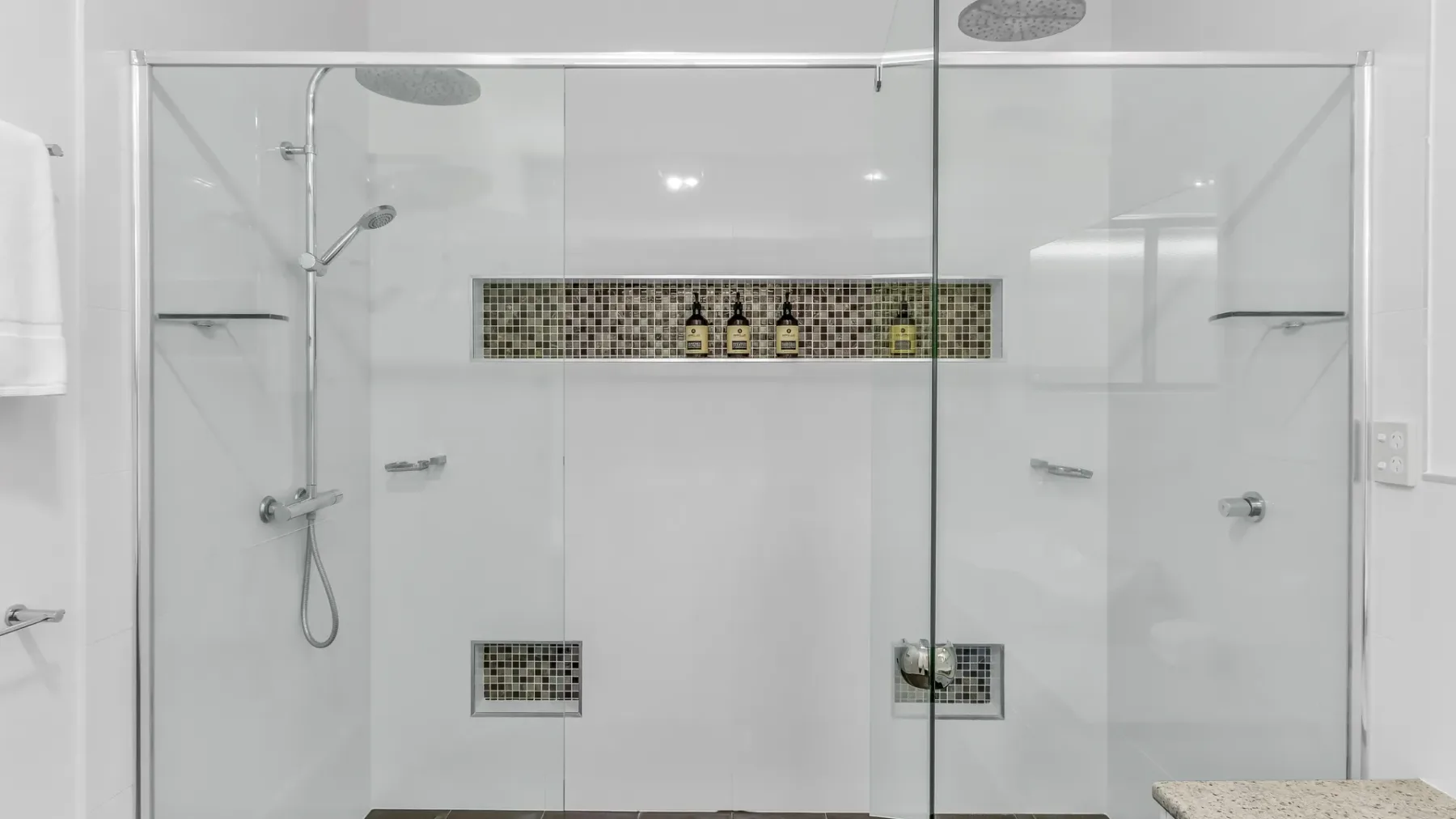 A white tiled bathroom shower with glass panels and a recessed shelf.