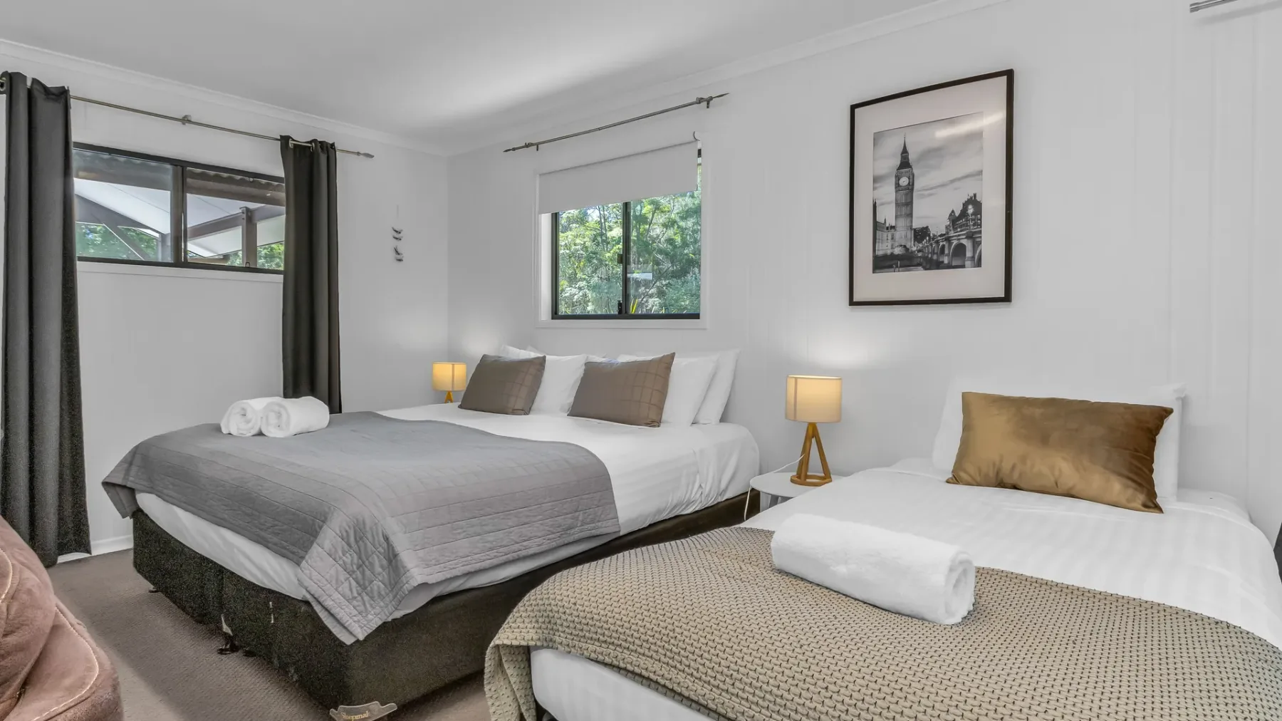 A bedroom with two beds, neutral bedding, and bedside lamps.