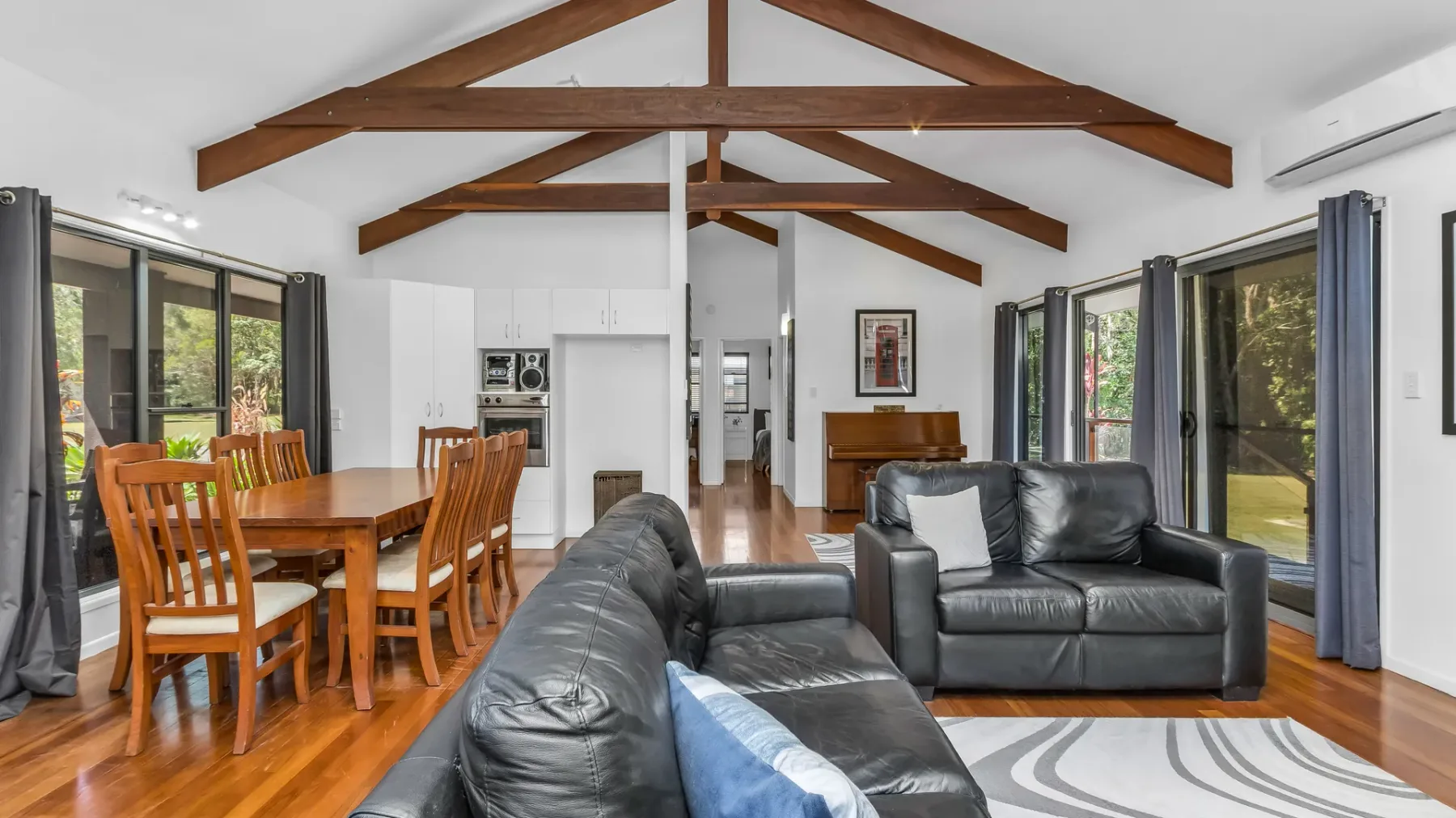 A bright open-plan living and dining room with exposed wooden ceiling beams.