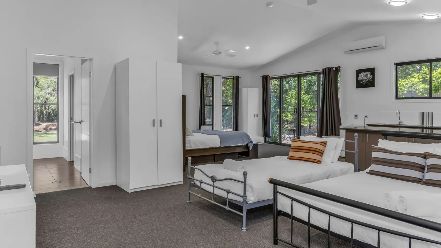 A bright bedroom with several beds and large windows overlooking greenery.