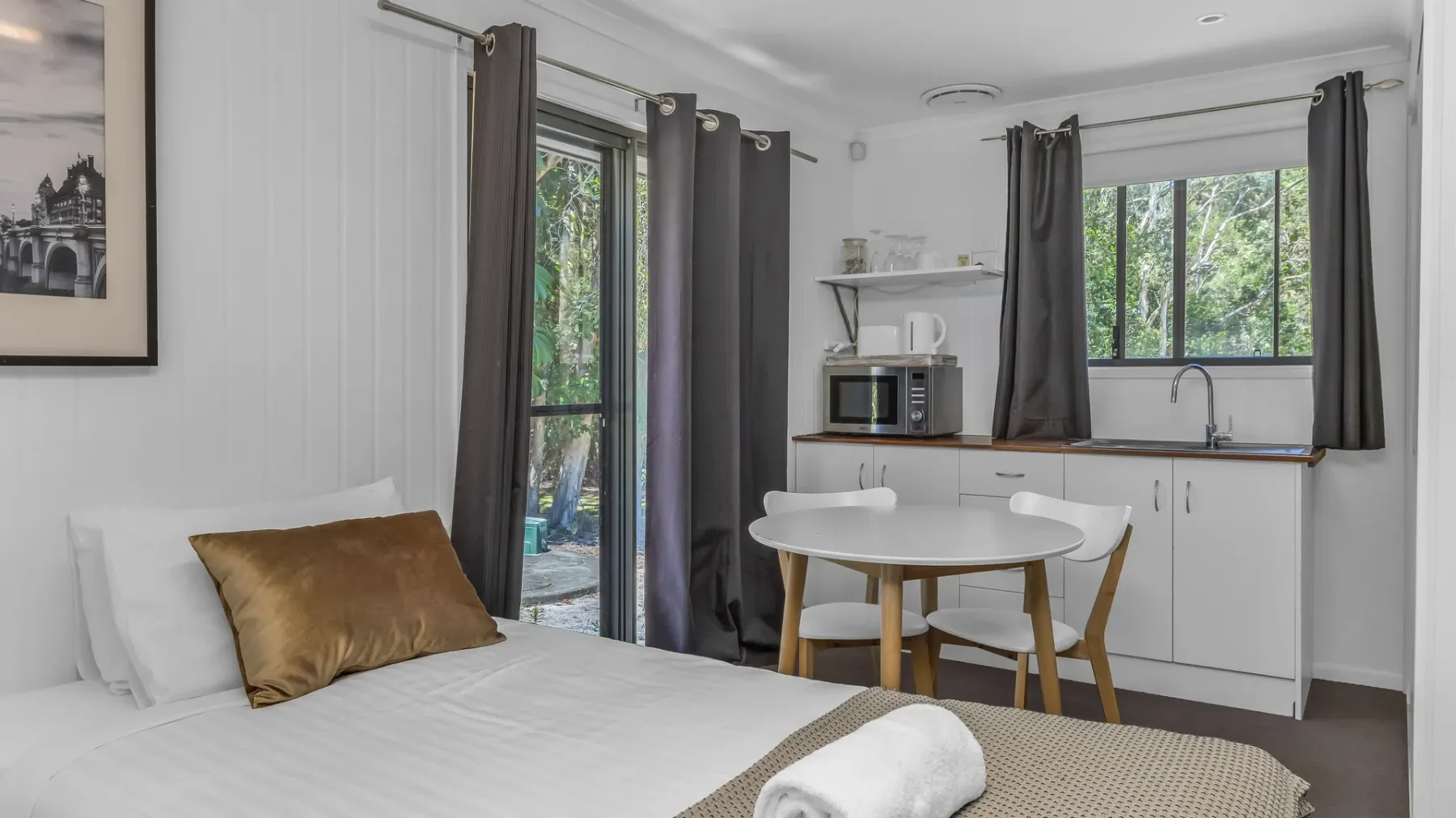 A bright studio room combines a bed and dining area beside a kitchenette.