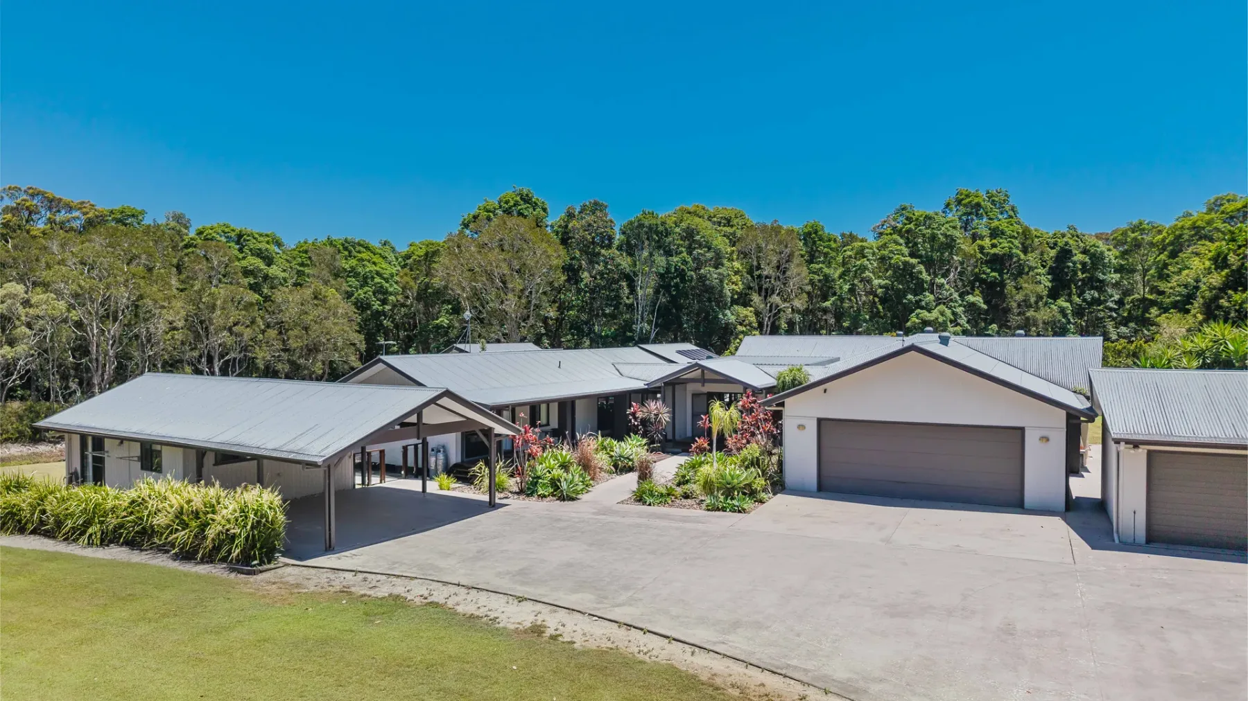 A group of low-rise buildings stands beside a broad paved driveway, with trees behind.