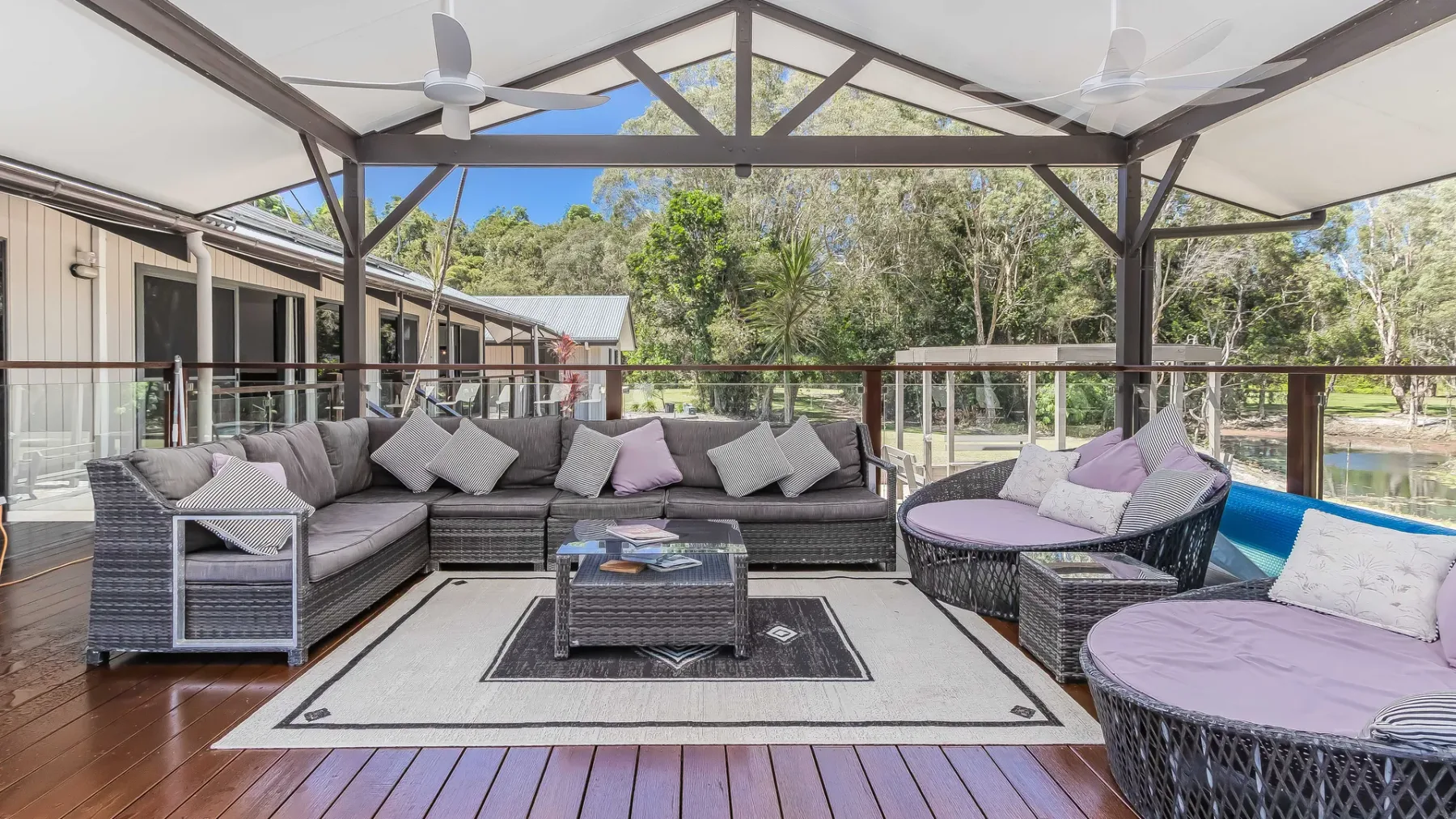 A covered outdoor seating area has cushioned furniture arranged around a low table.