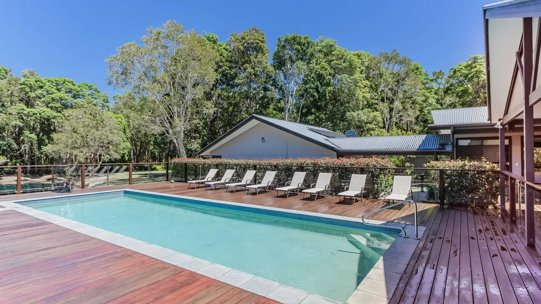An outdoor swimming pool is surrounded by a wooden deck and lounge seating.