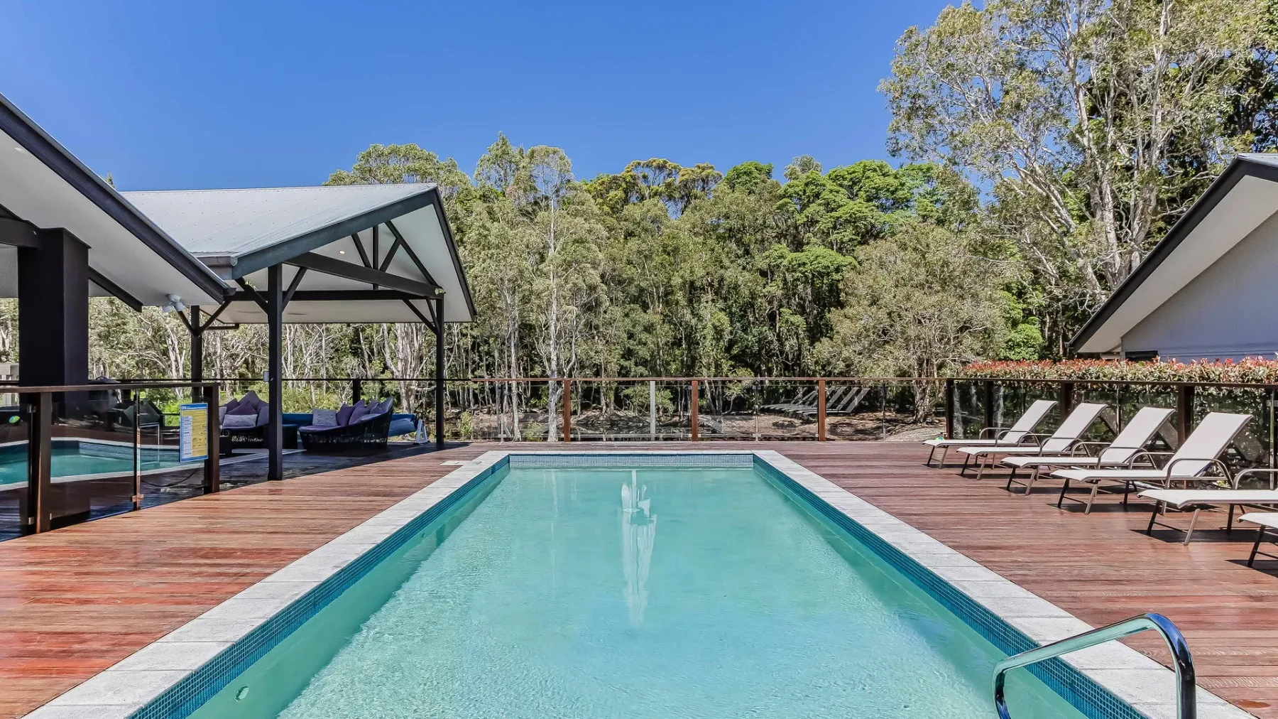 An outdoor swimming pool is surrounded by a wooden deck and lounge seating.
