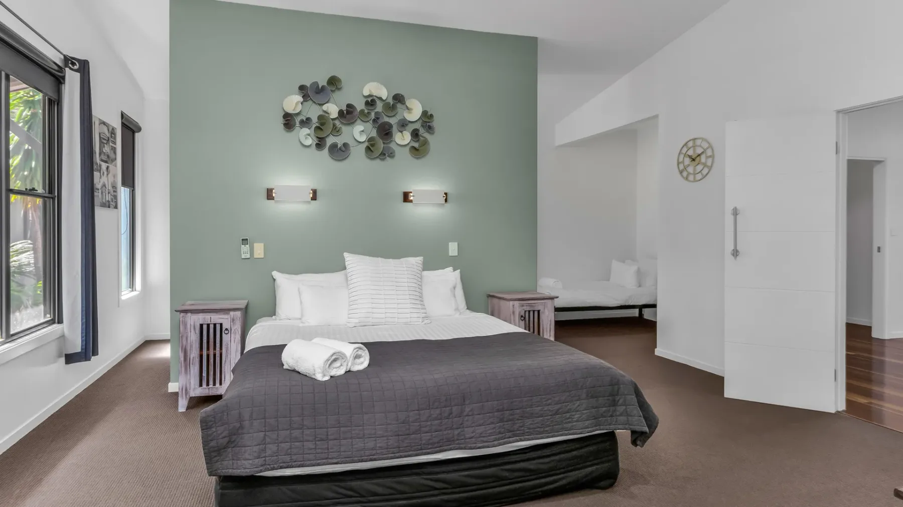 A bedroom with a neatly made bed and a pale green accent wall.