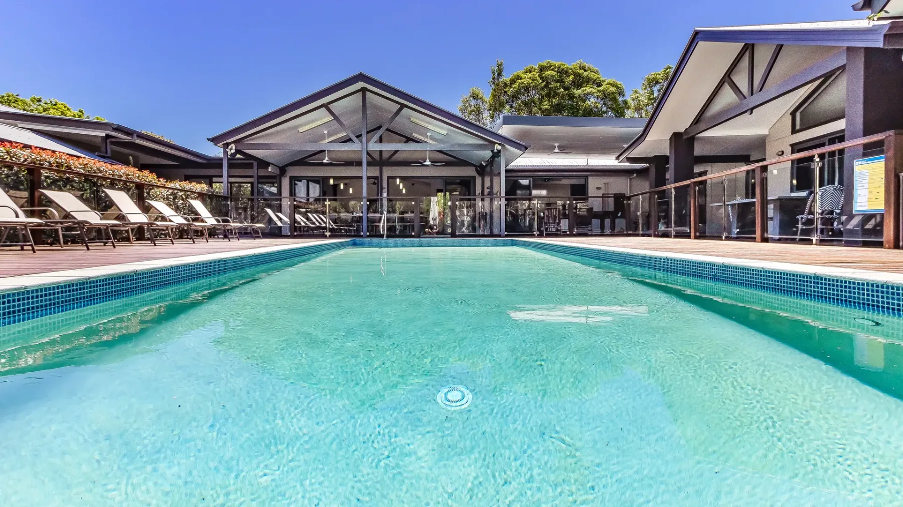 An outdoor swimming pool in front of a glass-fronted building and poolside seating.