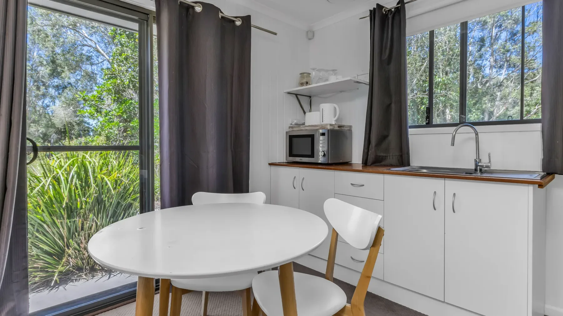 A bright kitchen with a round table and large windows overlooking greenery.