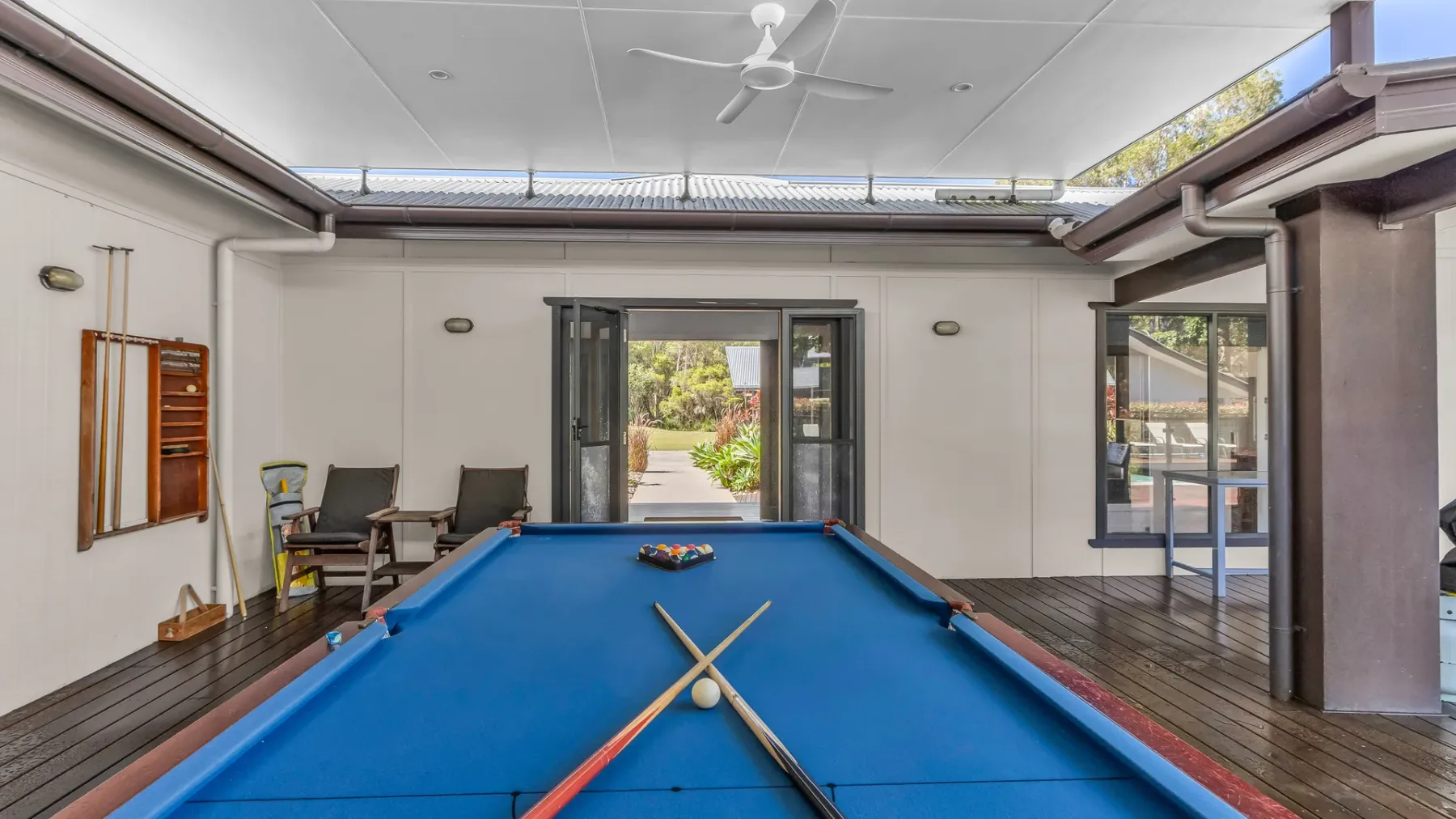 A pool table fills a bright open recreation room with doors opening to a garden.