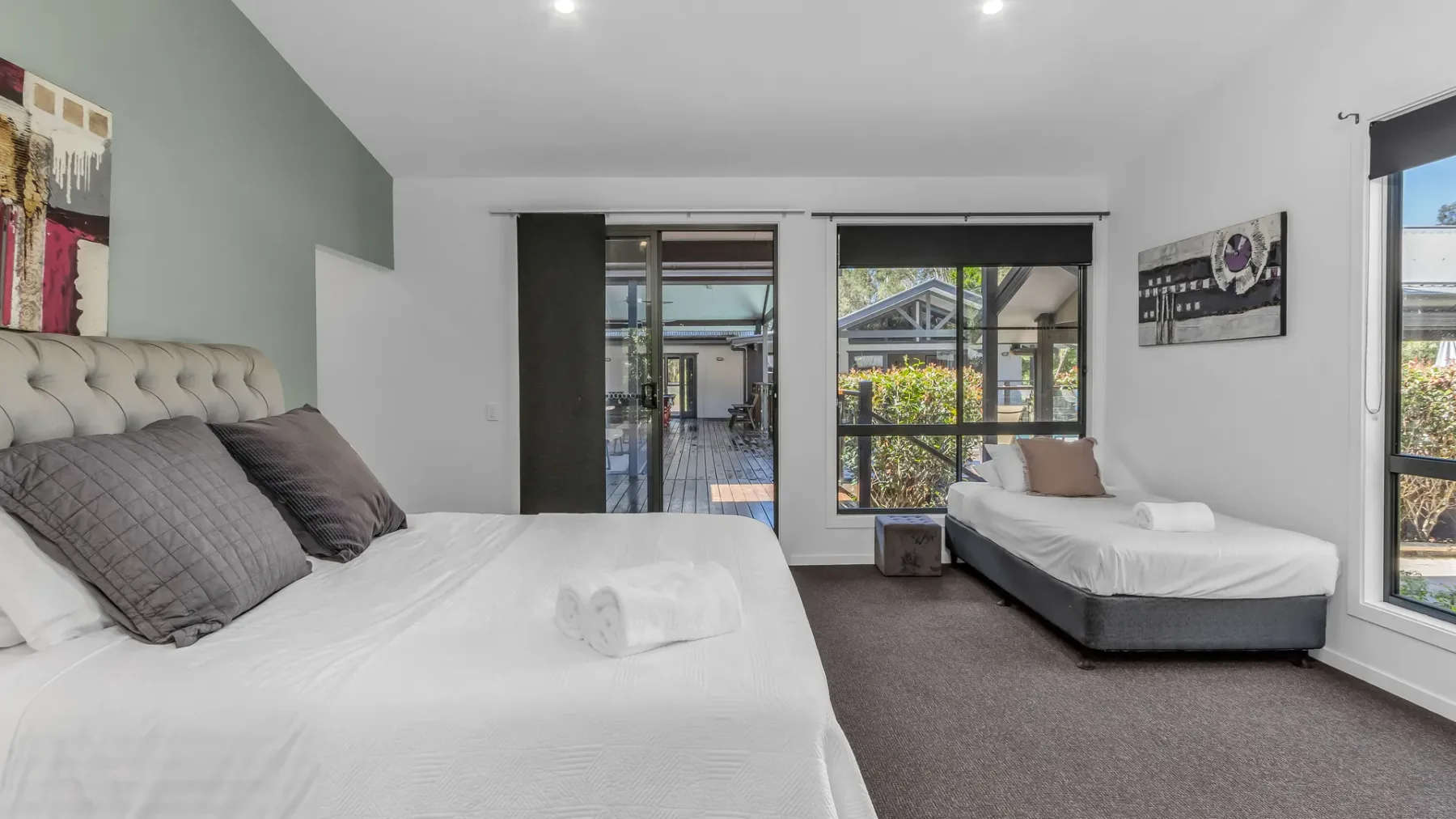 A bright bedroom with two beds and large windows overlooking greenery.