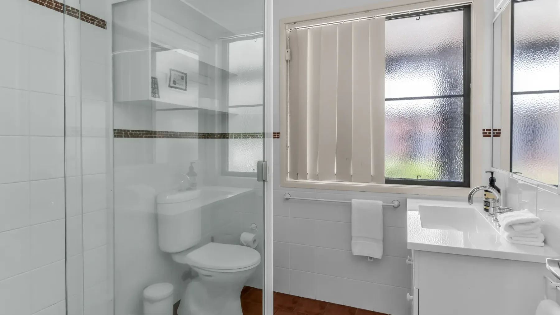 A bathroom with a shower, toilet, and sink beneath a window.