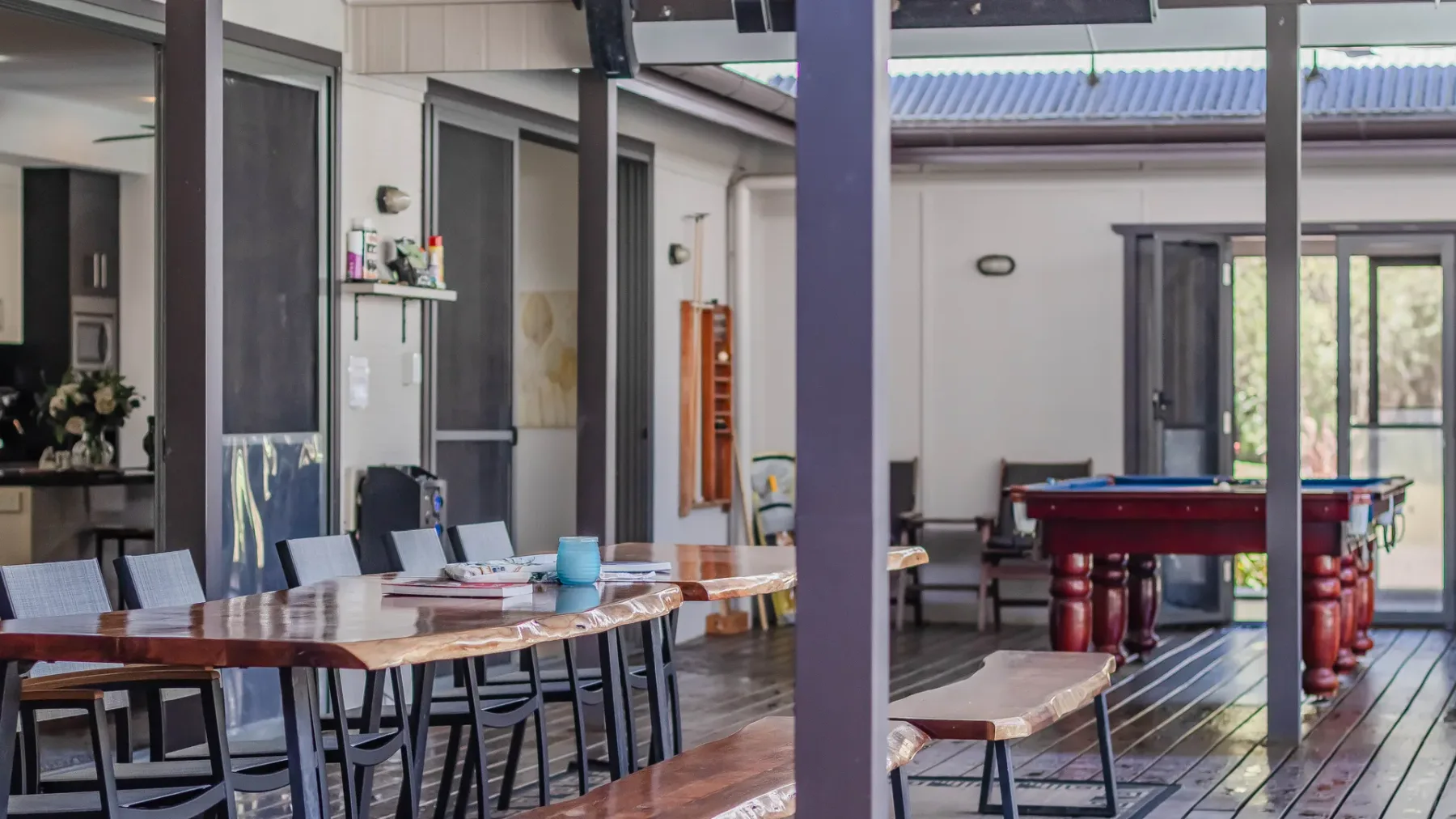 A covered patio dining area with a long table and a pool table beyond it.