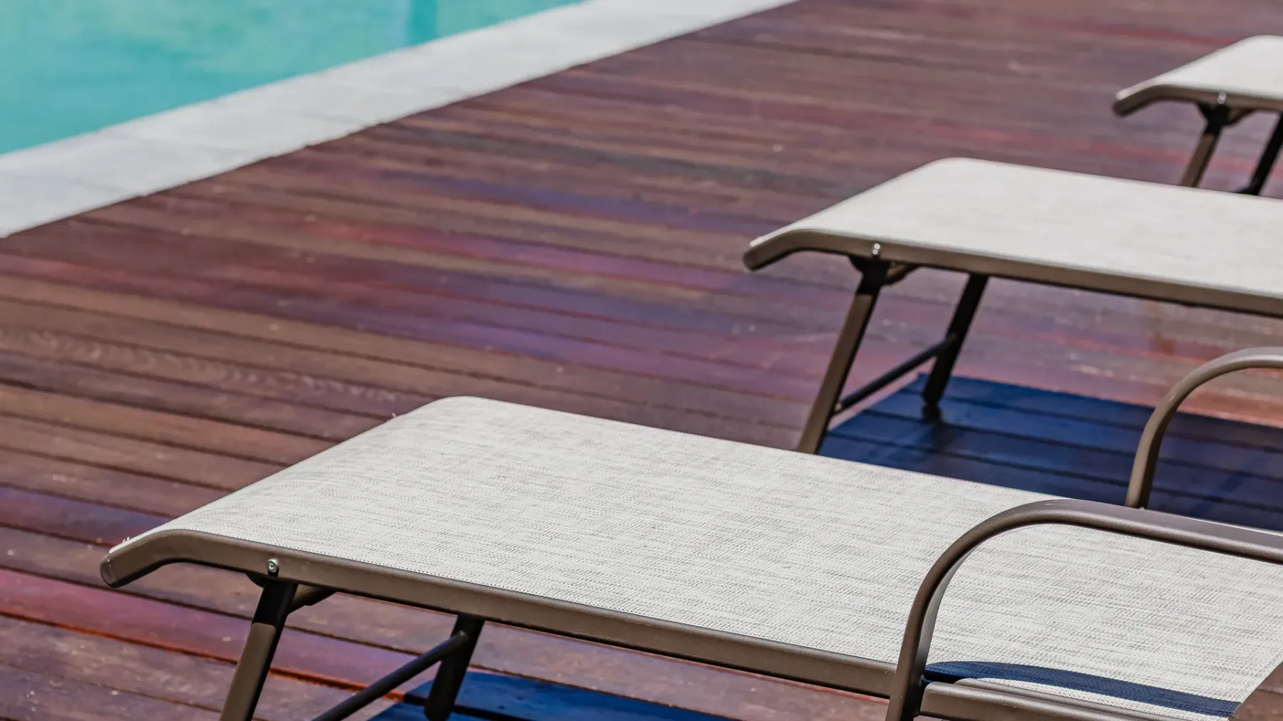 Poolside seating sits on a wooden deck beside turquoise water.