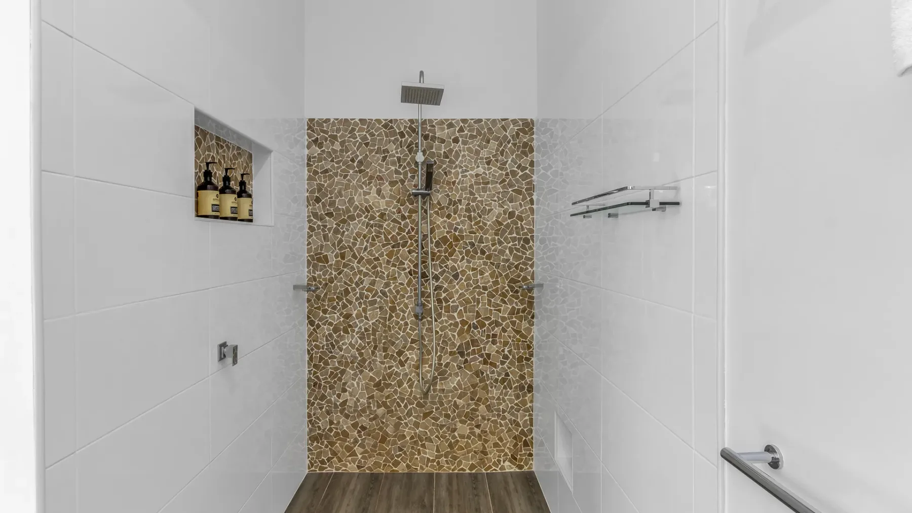 A tiled shower area with a patterned accent wall and wall-mounted shower fixtures.