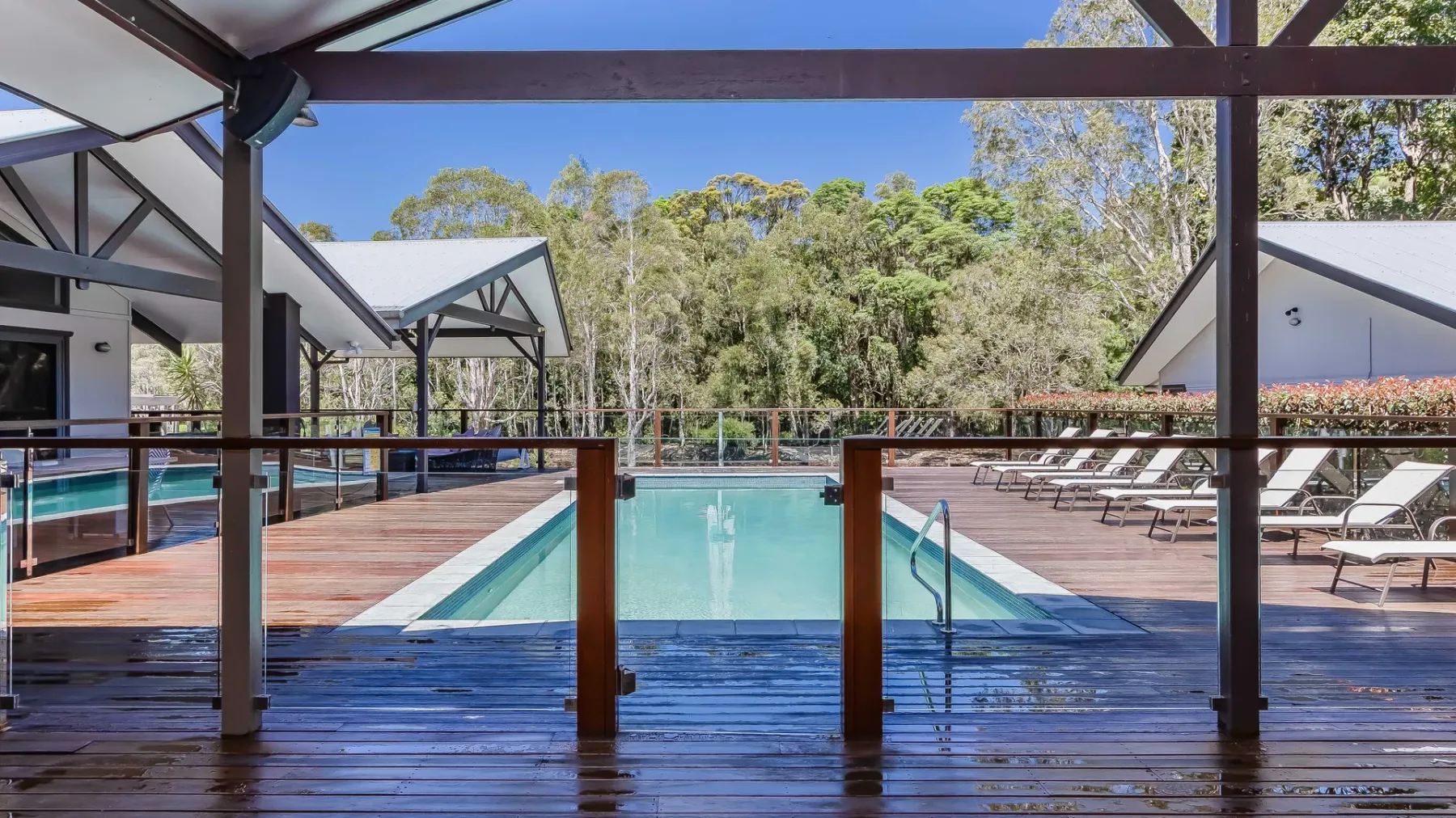 An outdoor swimming pool is surrounded by wooden decking and lounge chairs.