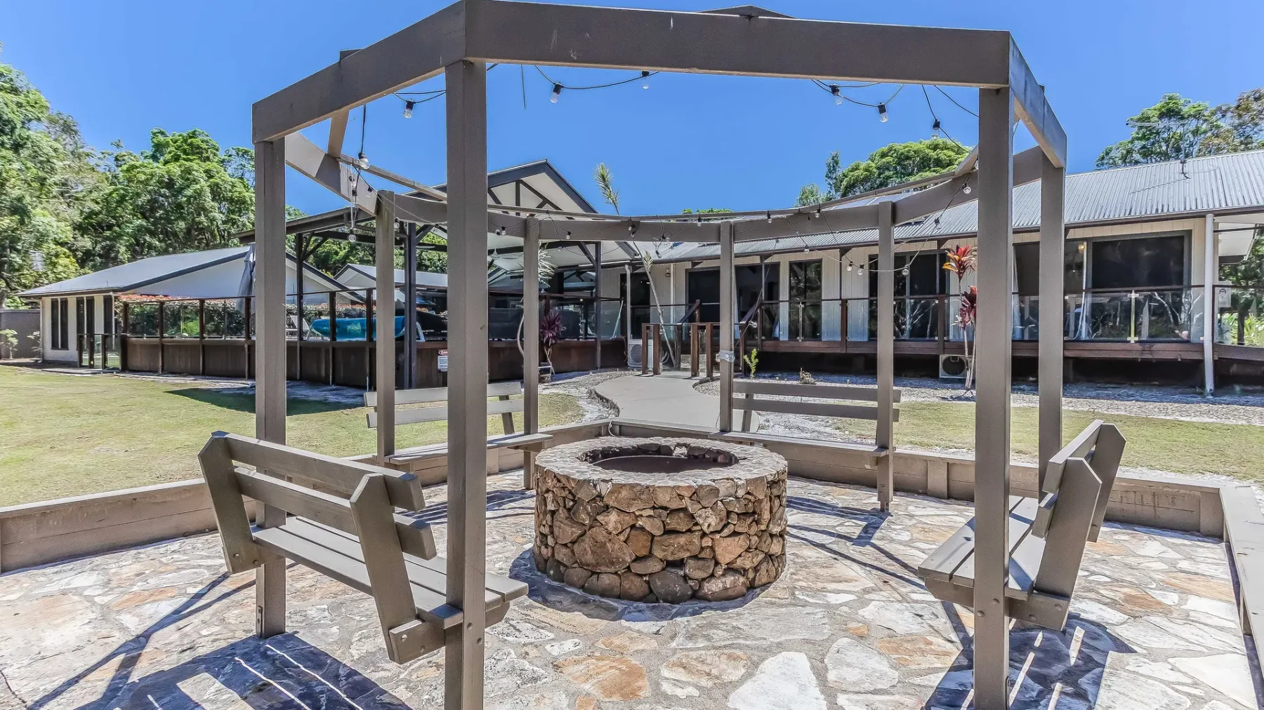 An outdoor courtyard features a stone fire pit beneath a wooden pergola.