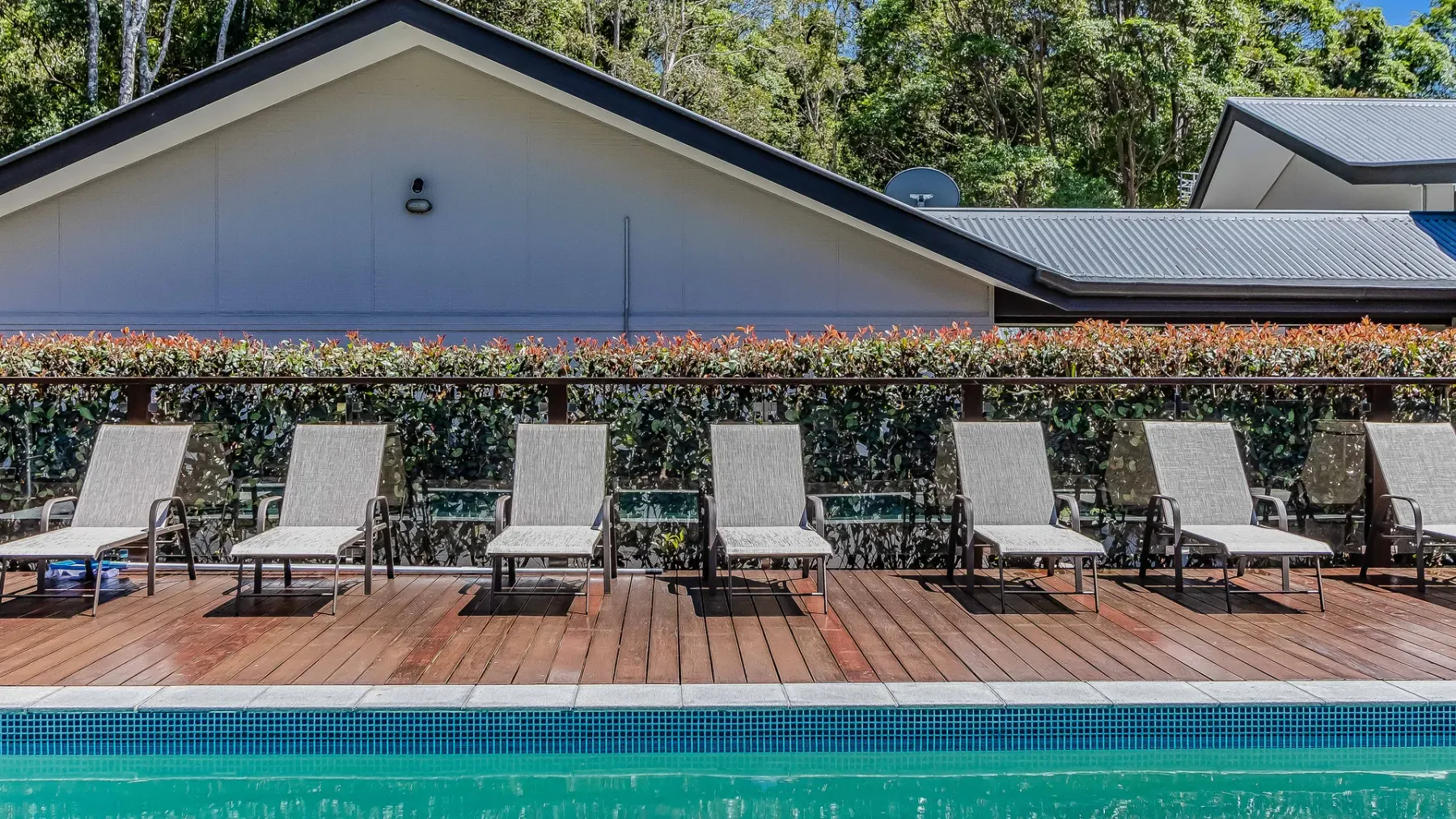 An outdoor pool borders a wooden deck lined with lounge seating.