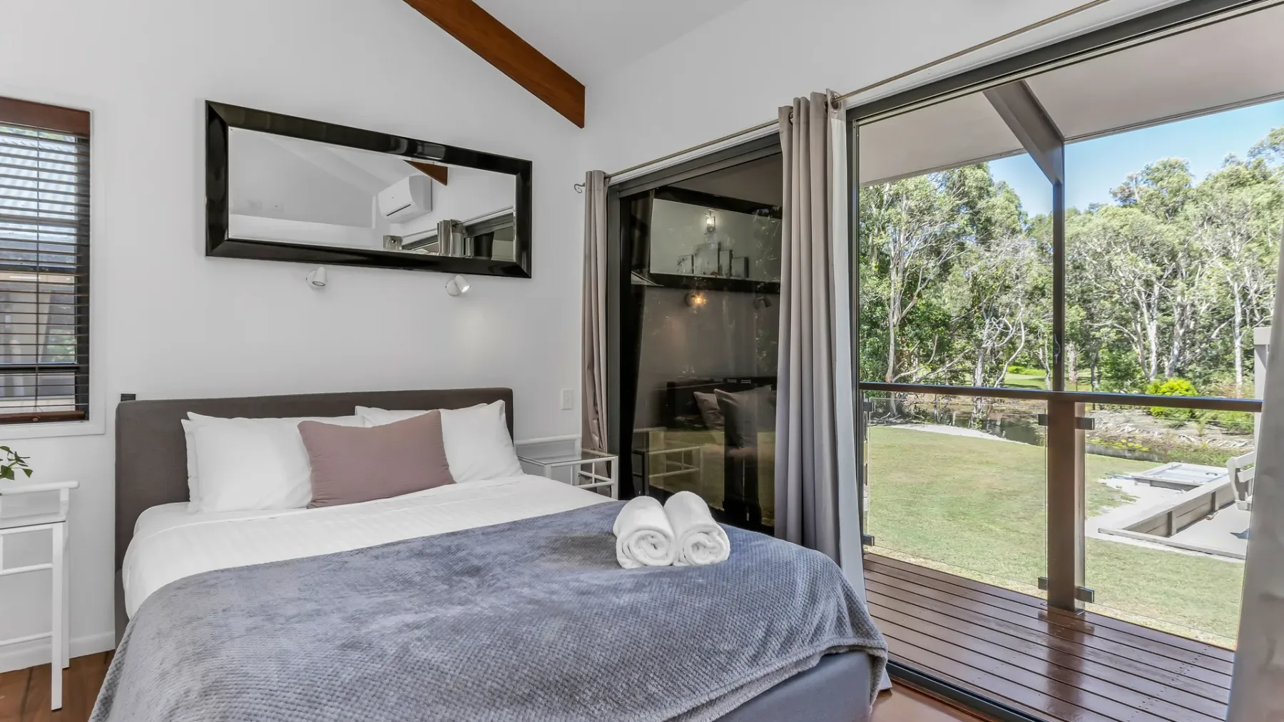 A bedroom with a neatly made bed beside sliding glass doors overlooking a garden.