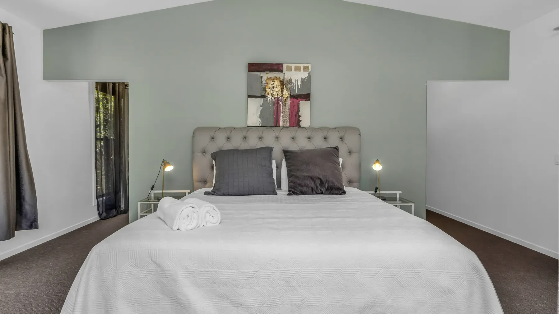 A bedroom with a neatly made bed and two pillows beneath a small wall artwork.