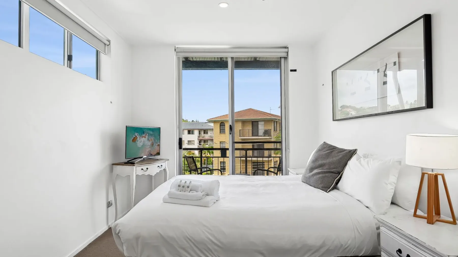 Un dormitorio luminoso con una cama bien tendida junto a una ventana grande.