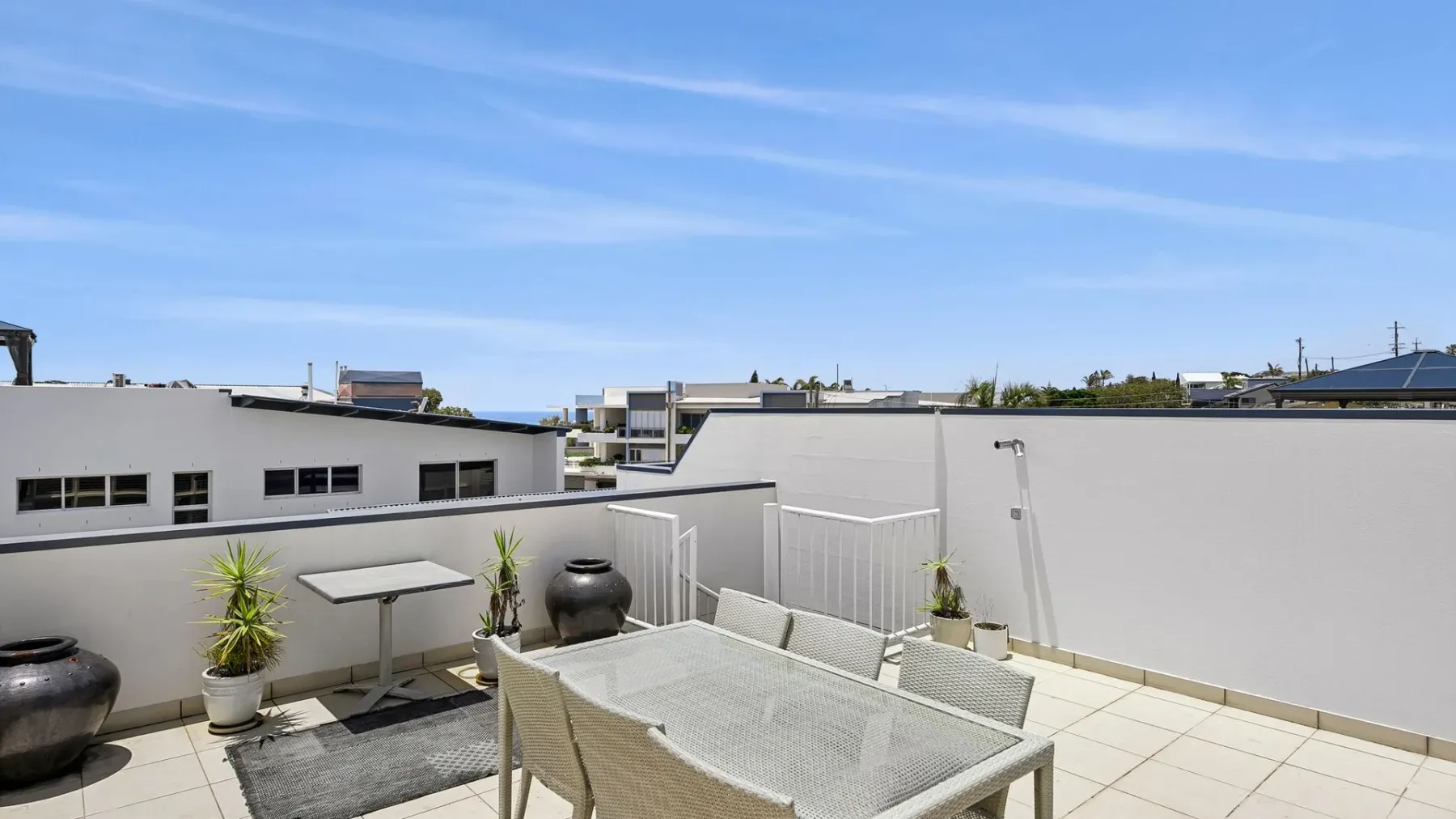 Una terraza en la azotea con una mesa de comedor y plantas en macetas bajo un cielo despejado.