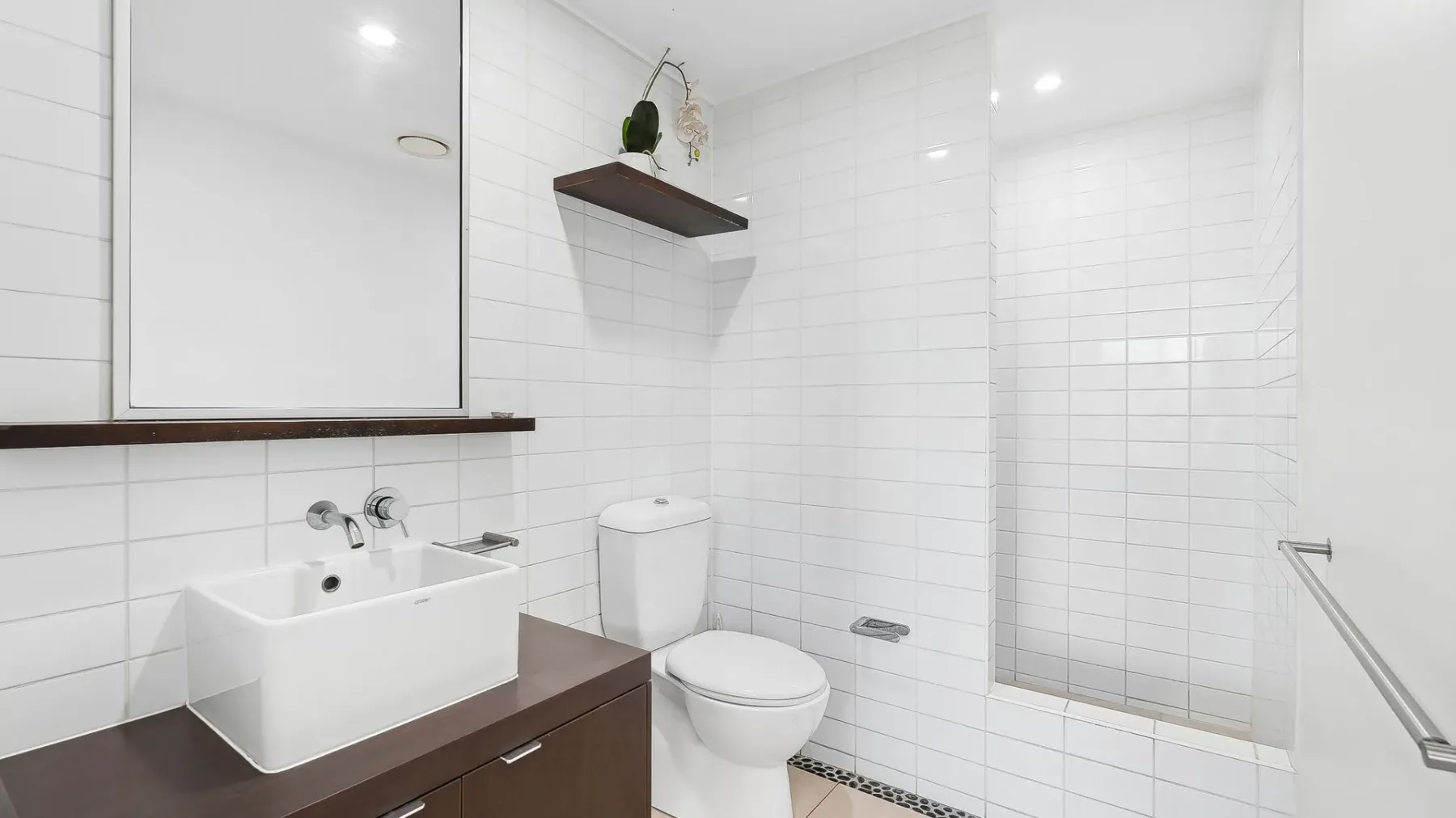 Un baño luminoso con azulejos, lavabo, inodoro y zona de ducha con vidrio.