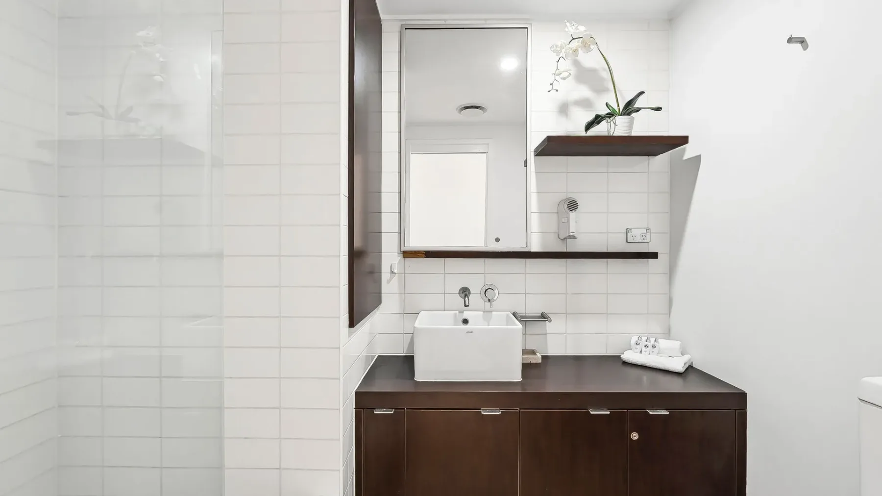 Un lavabo de baño con azulejos, un lavamanos blanco, espejo y una pequeña repisa.