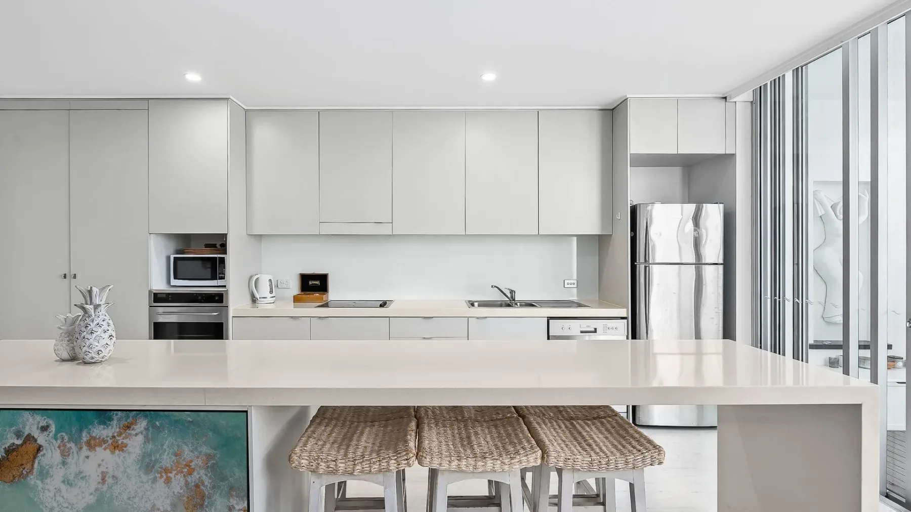 Una cocina moderna y luminosa con gabinetes blancos y una isla larga con bancos tejidos.