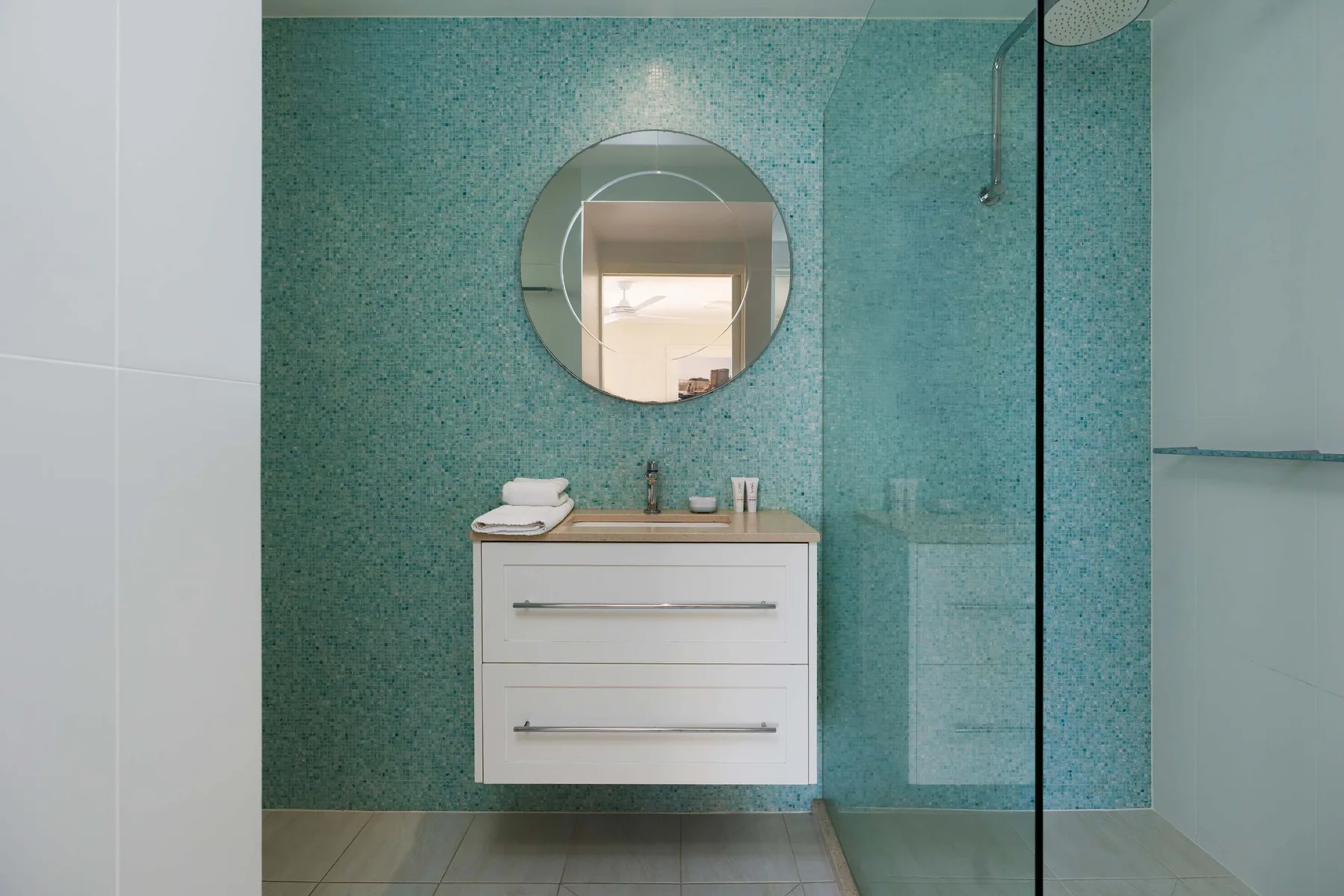 Un baño con un mueble blanco, un espejo redondo y una mampara de ducha de vidrio.