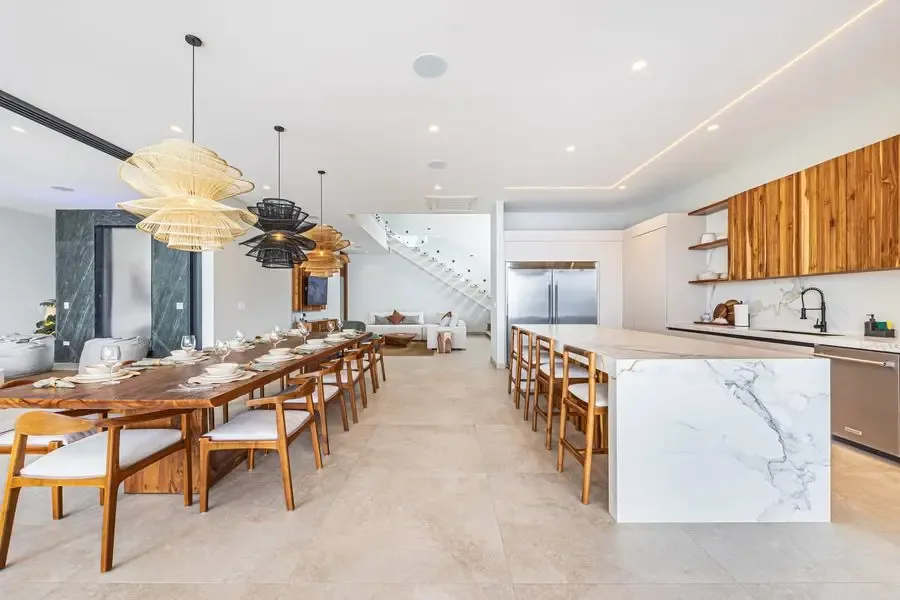 A bright open-plan dining and kitchen area with long wooden tables and an island.
