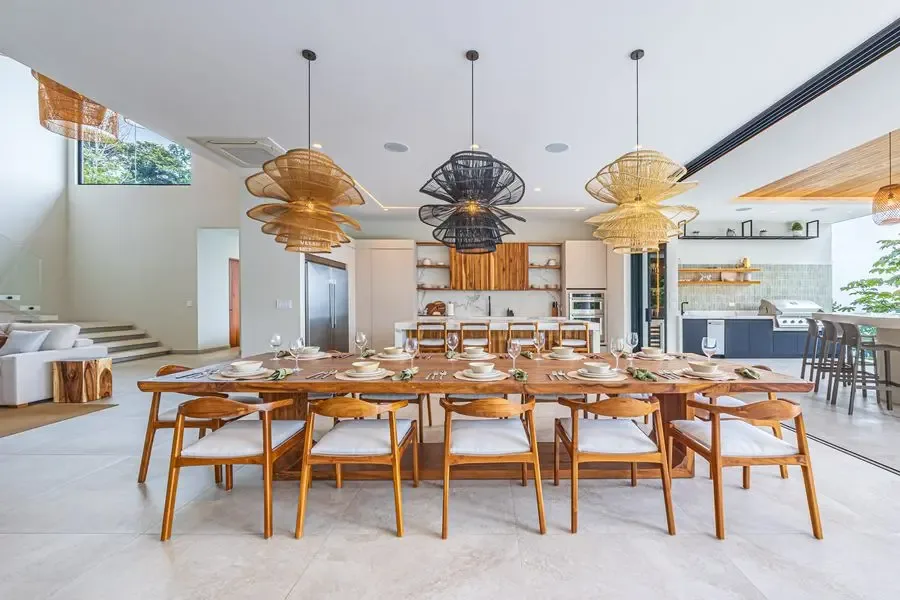 A dining area with a long wooden table and chairs beside an open kitchen.