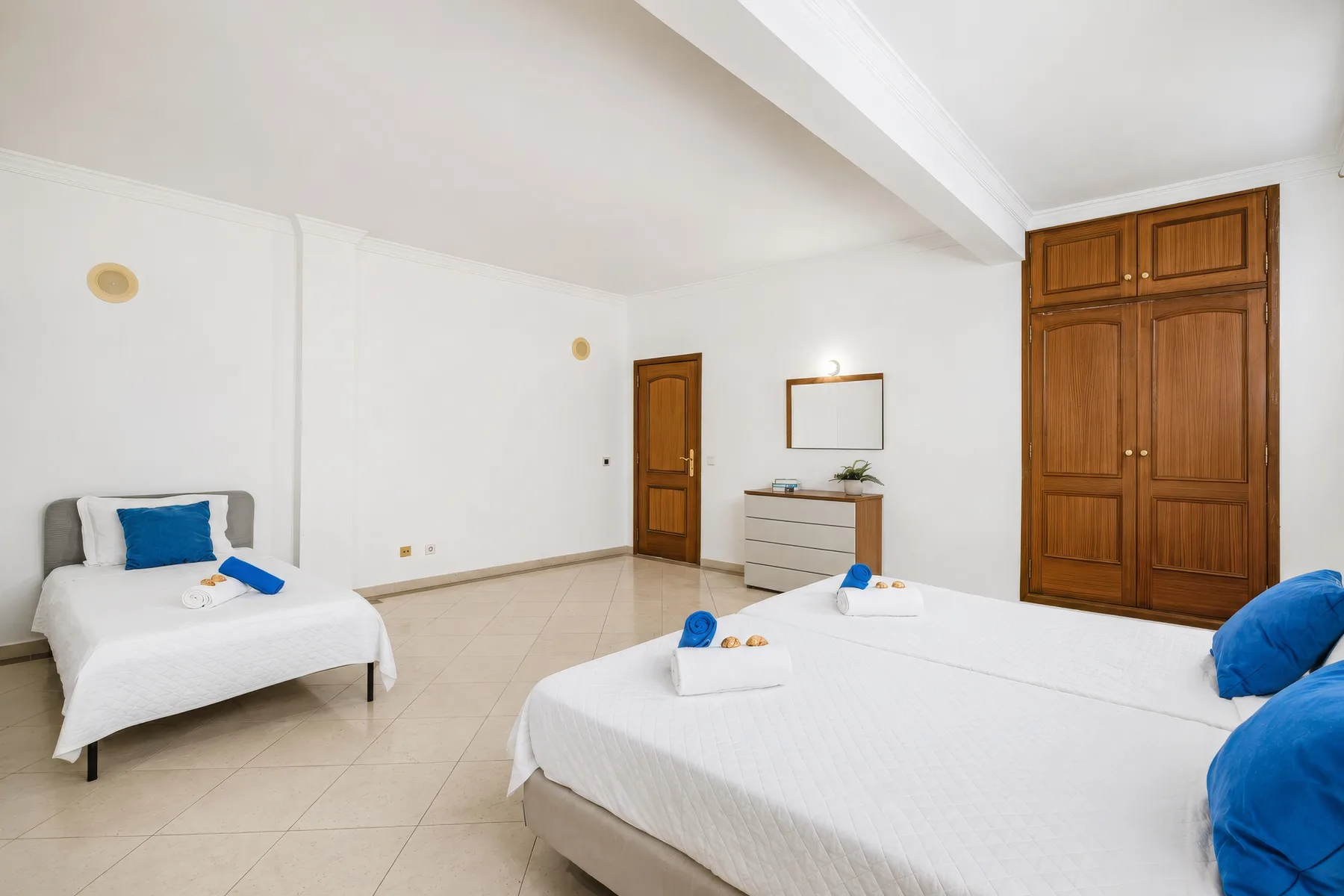 Un dormitorio luminoso con ropa de cama blanca, una cómoda y puertas de madera.