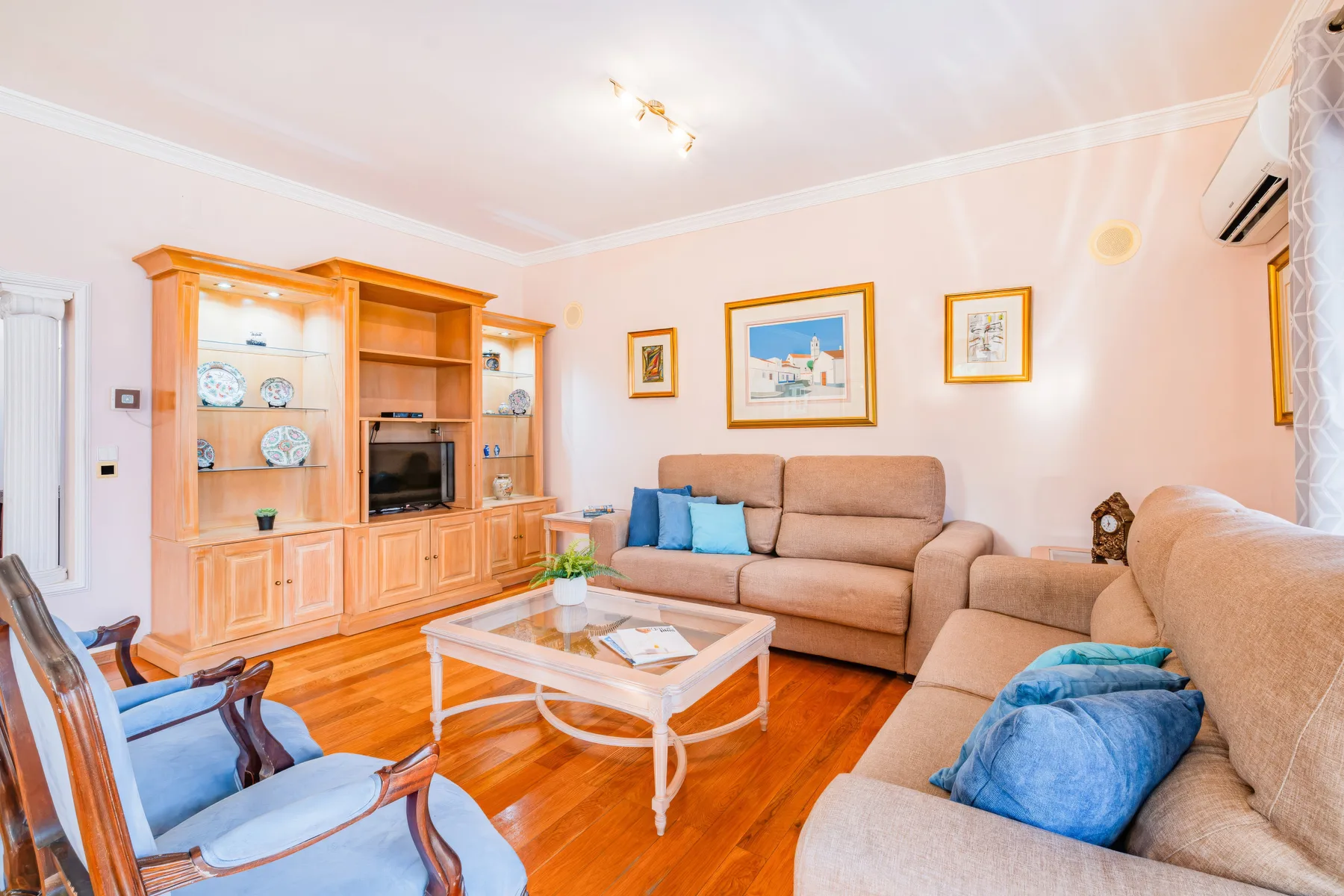 Una sala de estar con un sofá seccional beige, un mueble de madera y una mesa de centro de vidrio.