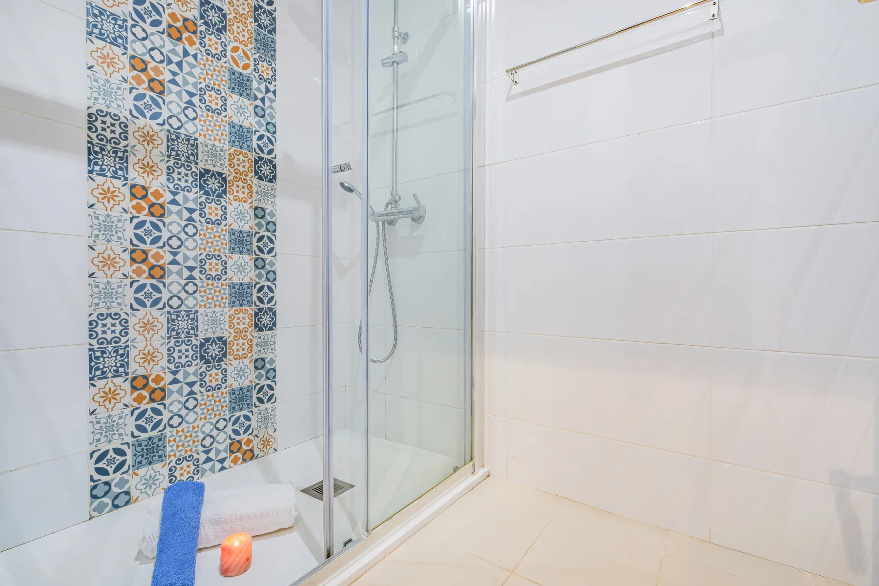 Un baño alicatado con una ducha de vidrio y azulejos decorativos.