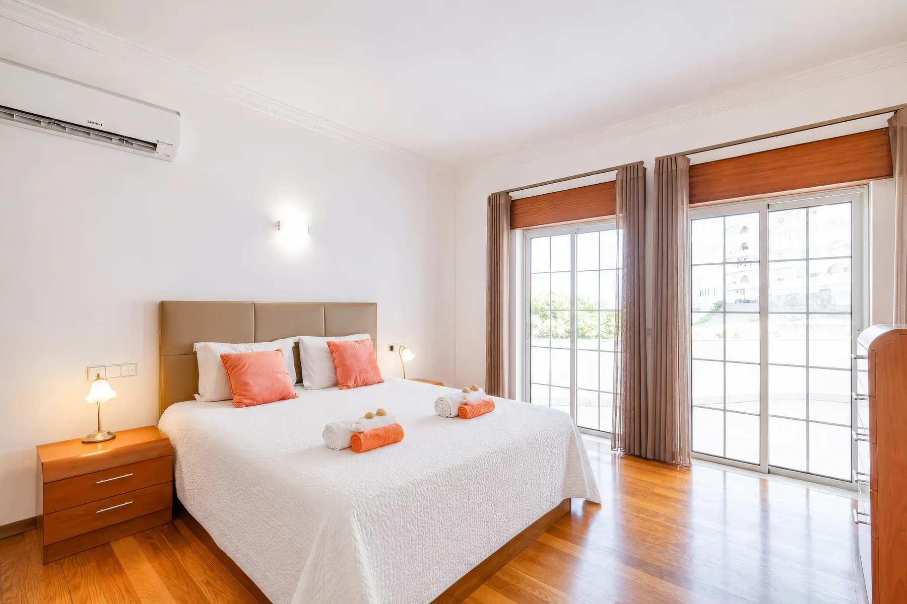 Un dormitorio luminoso con una cama bien hecha junto a grandes ventanas.