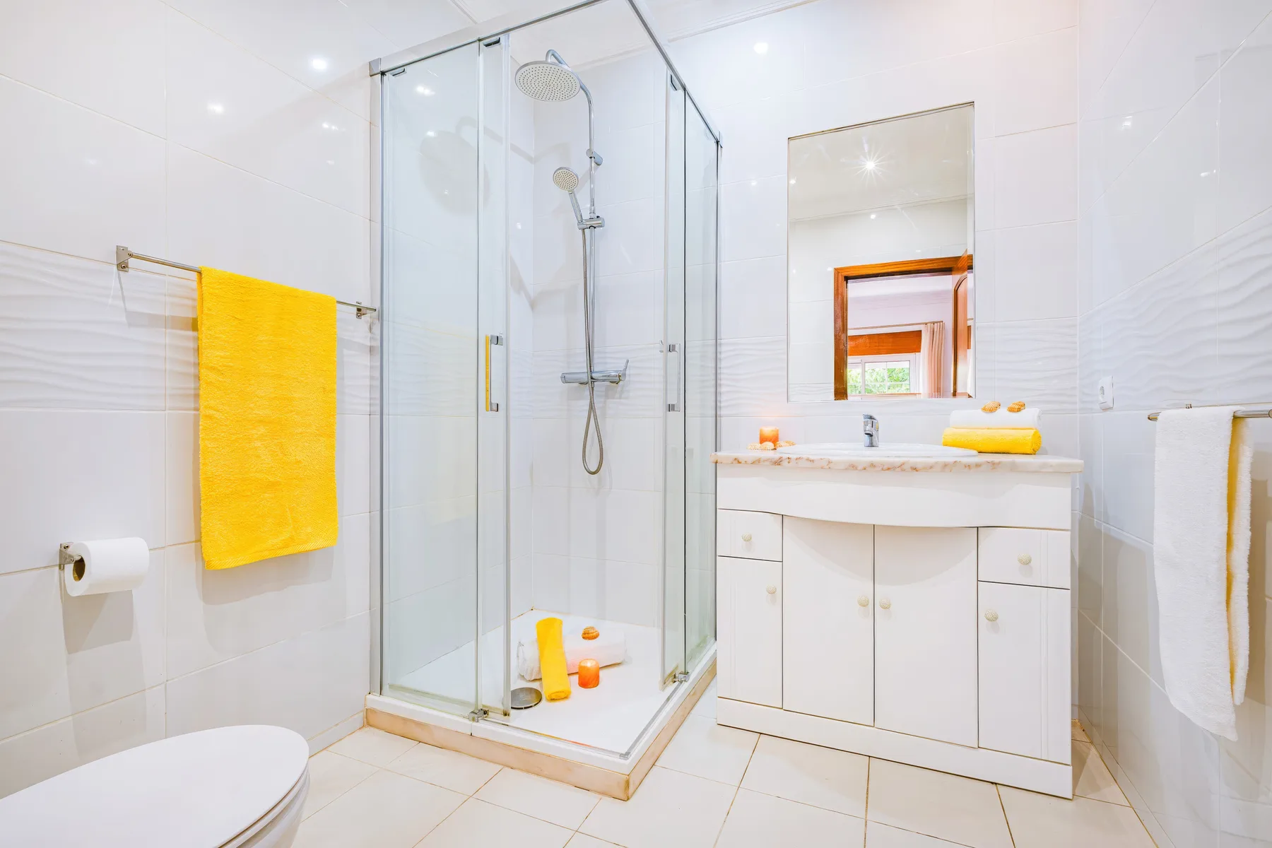 Un baño luminoso con ducha de vidrio y un tocador.