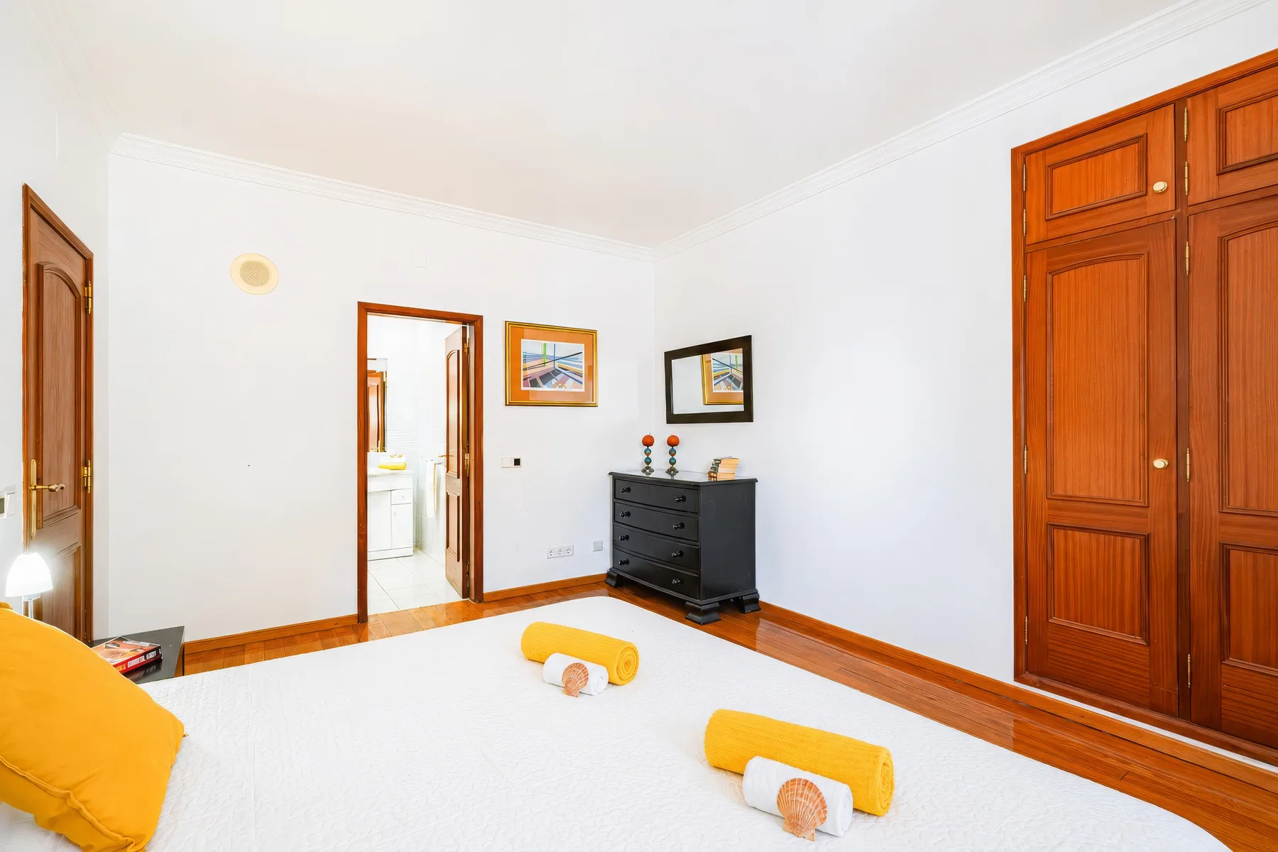 Un dormitorio luminoso con una cama blanca, toallas dobladas y puertas de madera.