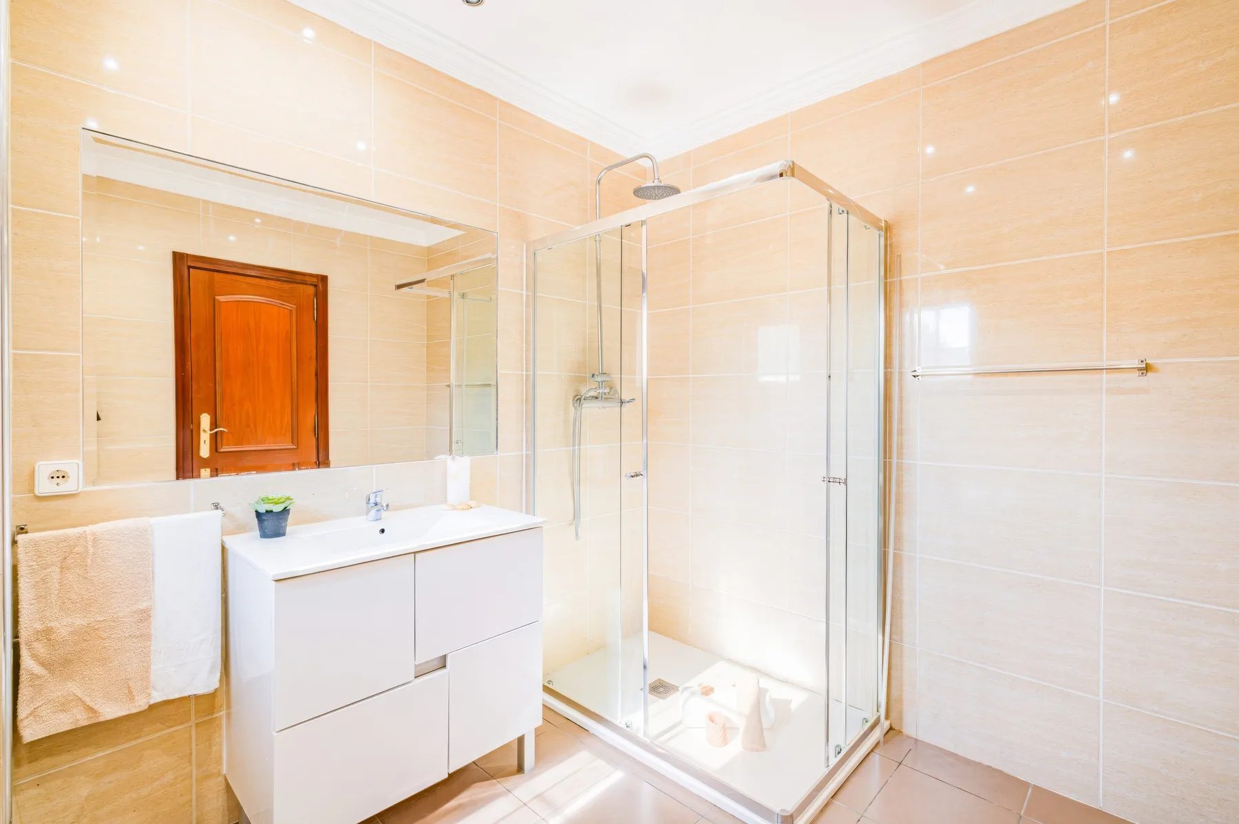 Un baño luminoso con azulejos, lavabo y ducha de vidrio.