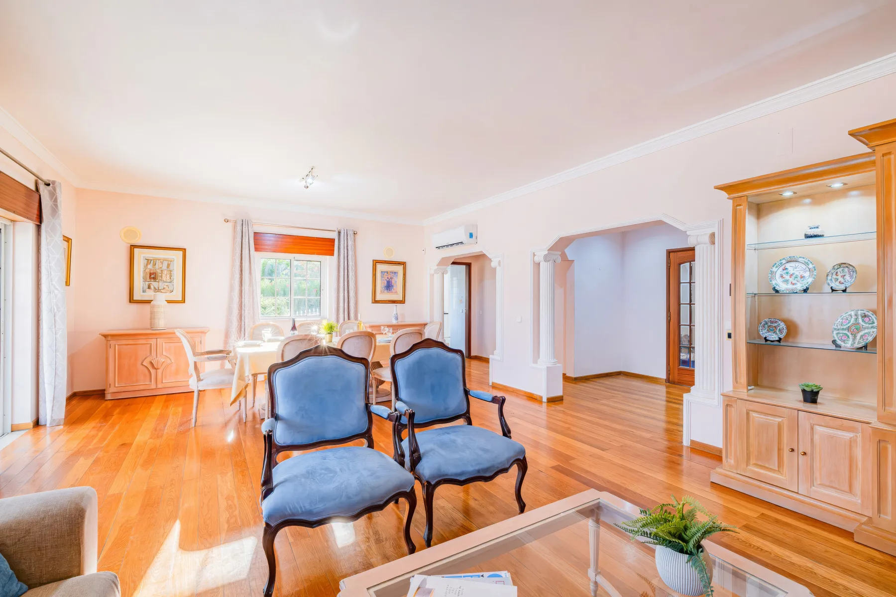 Una sala luminosa con asientos azules, una mesa de centro de vidrio y un mueble de exhibición de madera.