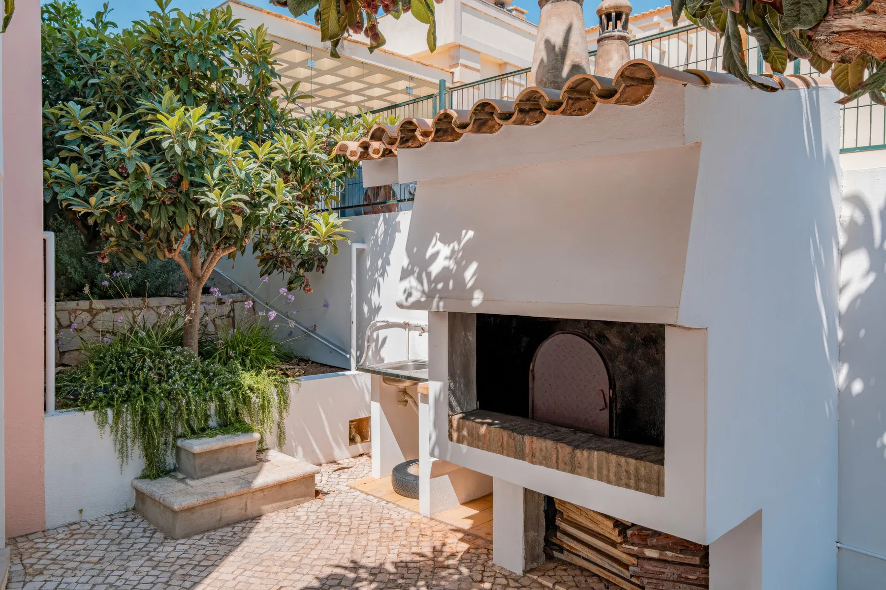 Un patio pavimentado con una barbacoa integrada y plantas frondosas.